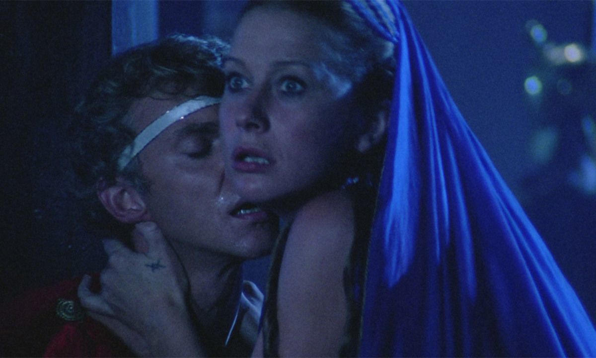 Ein Mann und eine Frau sind nah beieinander und wirken verstört. Die Frau trägt eine blaue Kopfbedeckung. Der Mann hat ein weißes Stirnband.