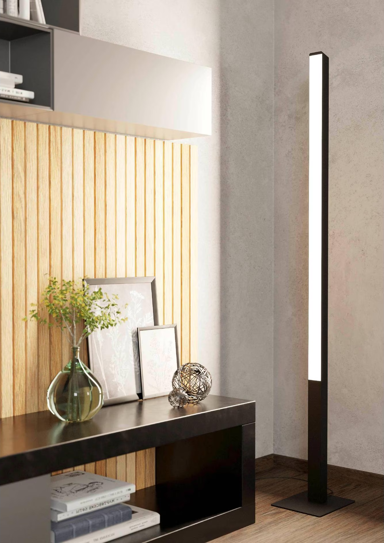 Un soggiorno moderno con tavolo nero, pianta, cornici, sfere decorative e una lampada alta illuminata.