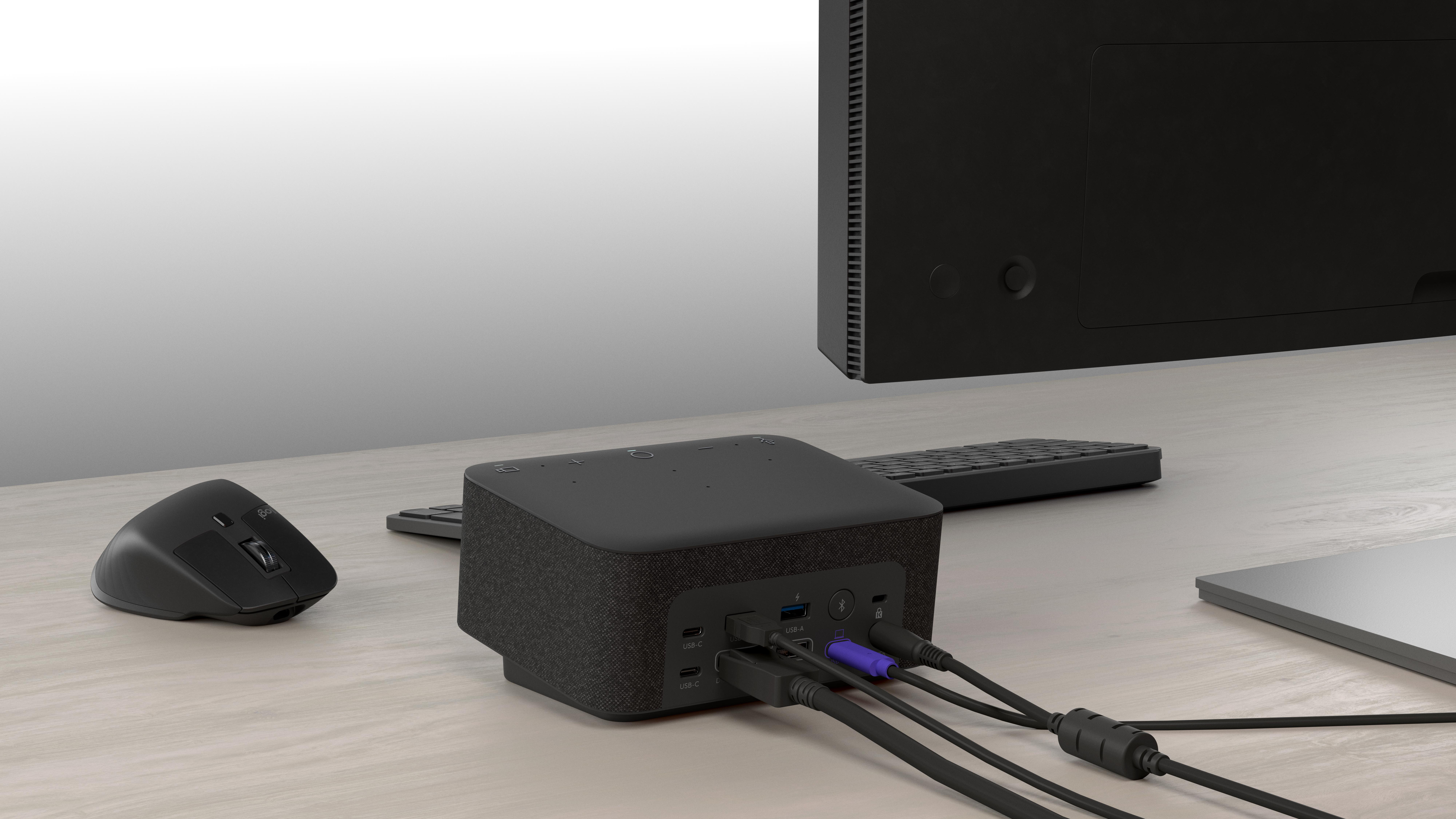 Eine schwarze Dockingstation mit angeschlossenen Kabeln auf einem Holztisch, eine Maus, Tastatur und Monitor sind ebenfalls vorhanden.