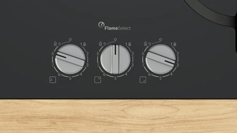 Primer plano de una placa de cocina negra con tres mandos. Logotipo FlameSelect arriba. Los mandos están numerados con iconos de llama.