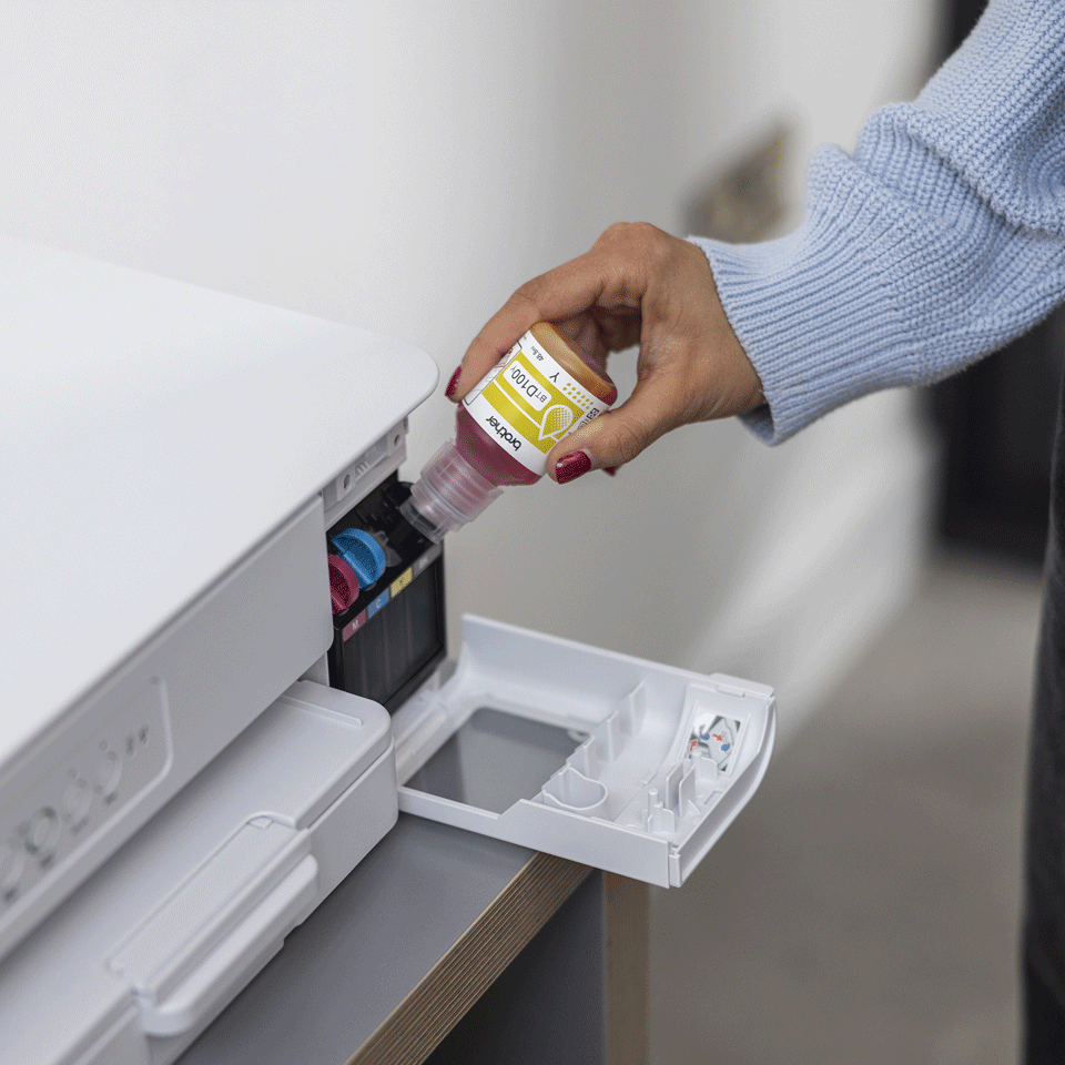 Osoba uzupełnia drukarkę różowym tuszem. Żółta butelka z tuszem wlewa tusz do zbiornika na tusz drukarki. Drukarka jest biała.