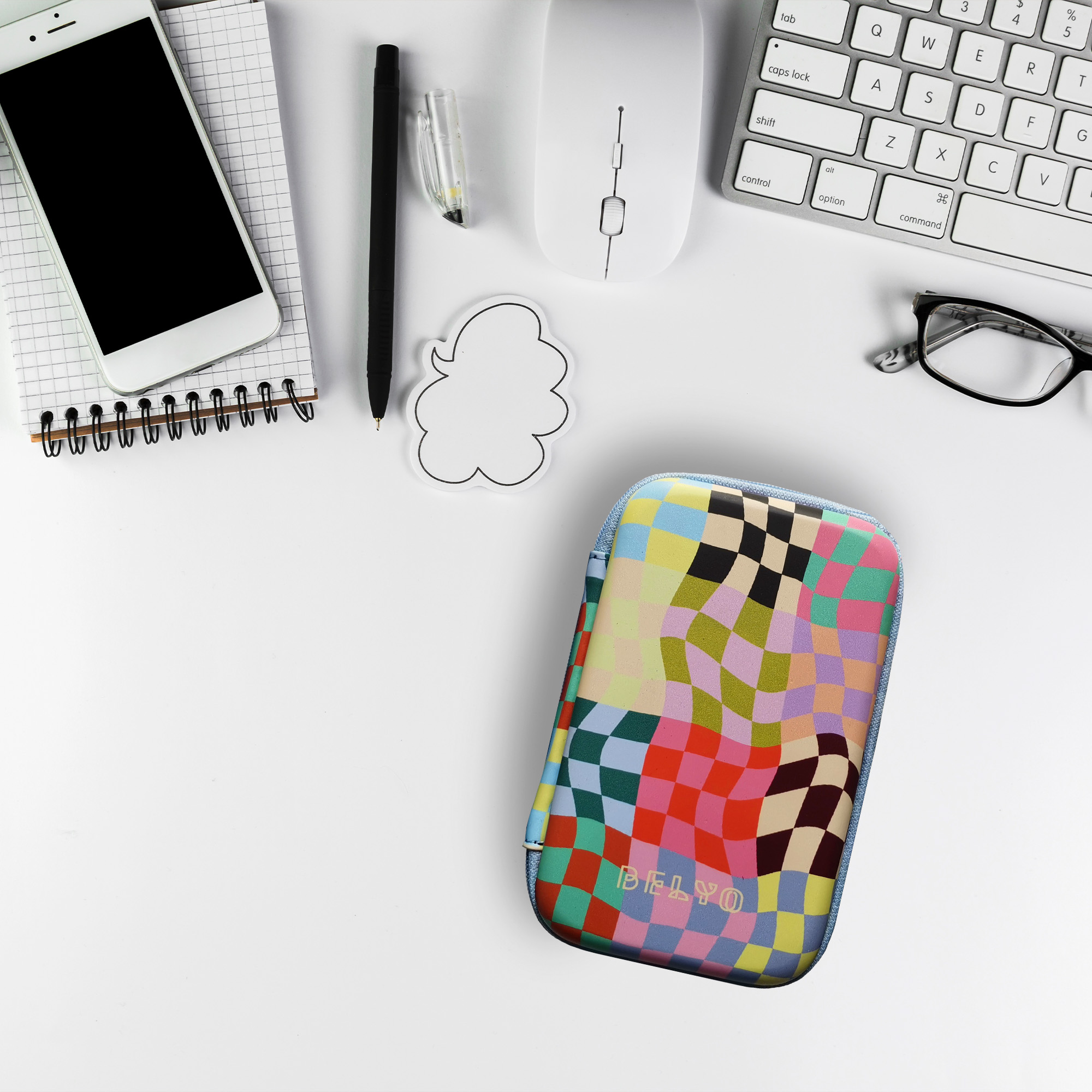 Escritorio blanco con teléfono, bolígrafo, ratón, teclado, gafas, bloc de notas y un estuche a cuadros de colores.