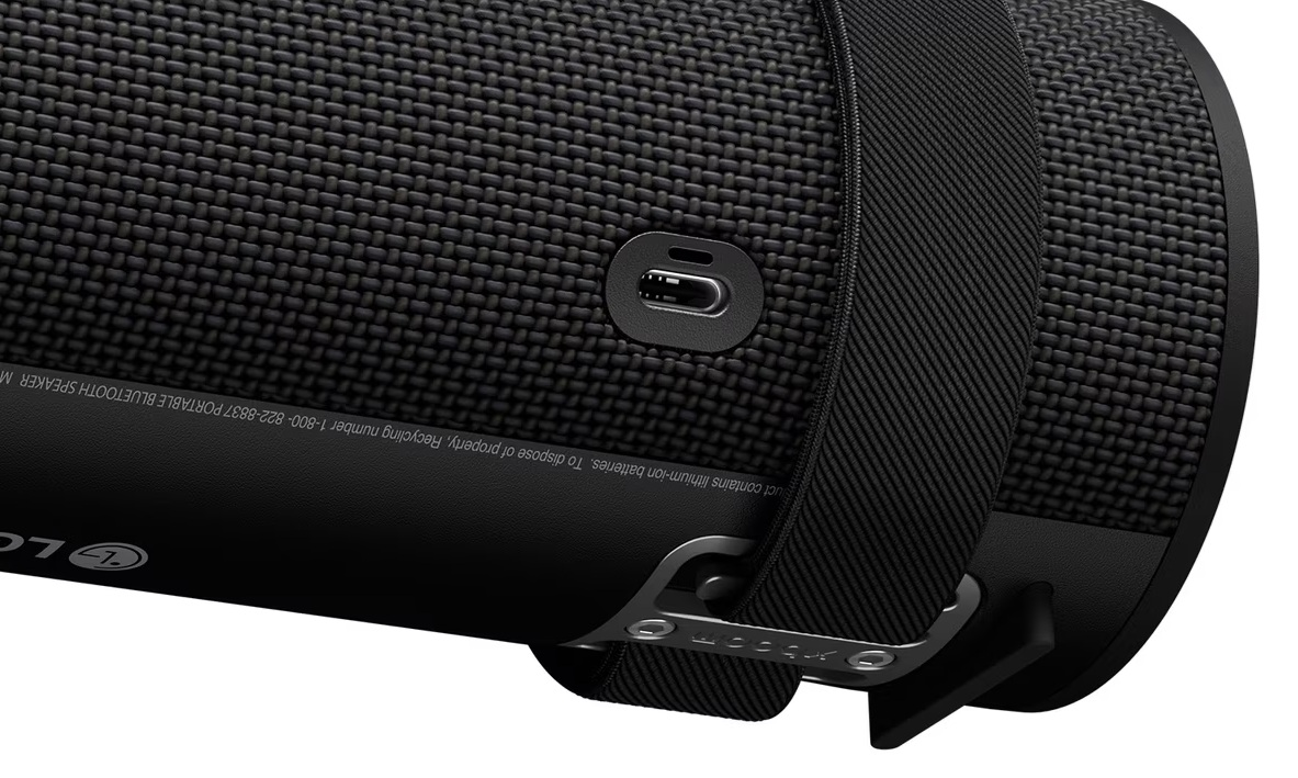 Zbliżenie czarnego głośnika przenośnego z tkaną teksturą i czarnym paskiem. Widoczny jest port USB-C.