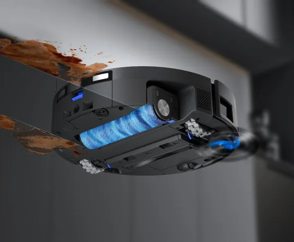 Czarny robot odkurzający czyszczący brudną powierzchnię. Ma niebieską szczotkę i jest otoczony rozpryskami brązowego brudu.