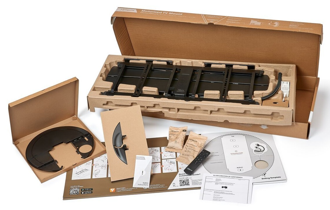 Otwarty karton z czarnym uchwytem do telewizora, akcesoriami, instrukcjami i pilotem. Brązowe opakowanie i białe tło.