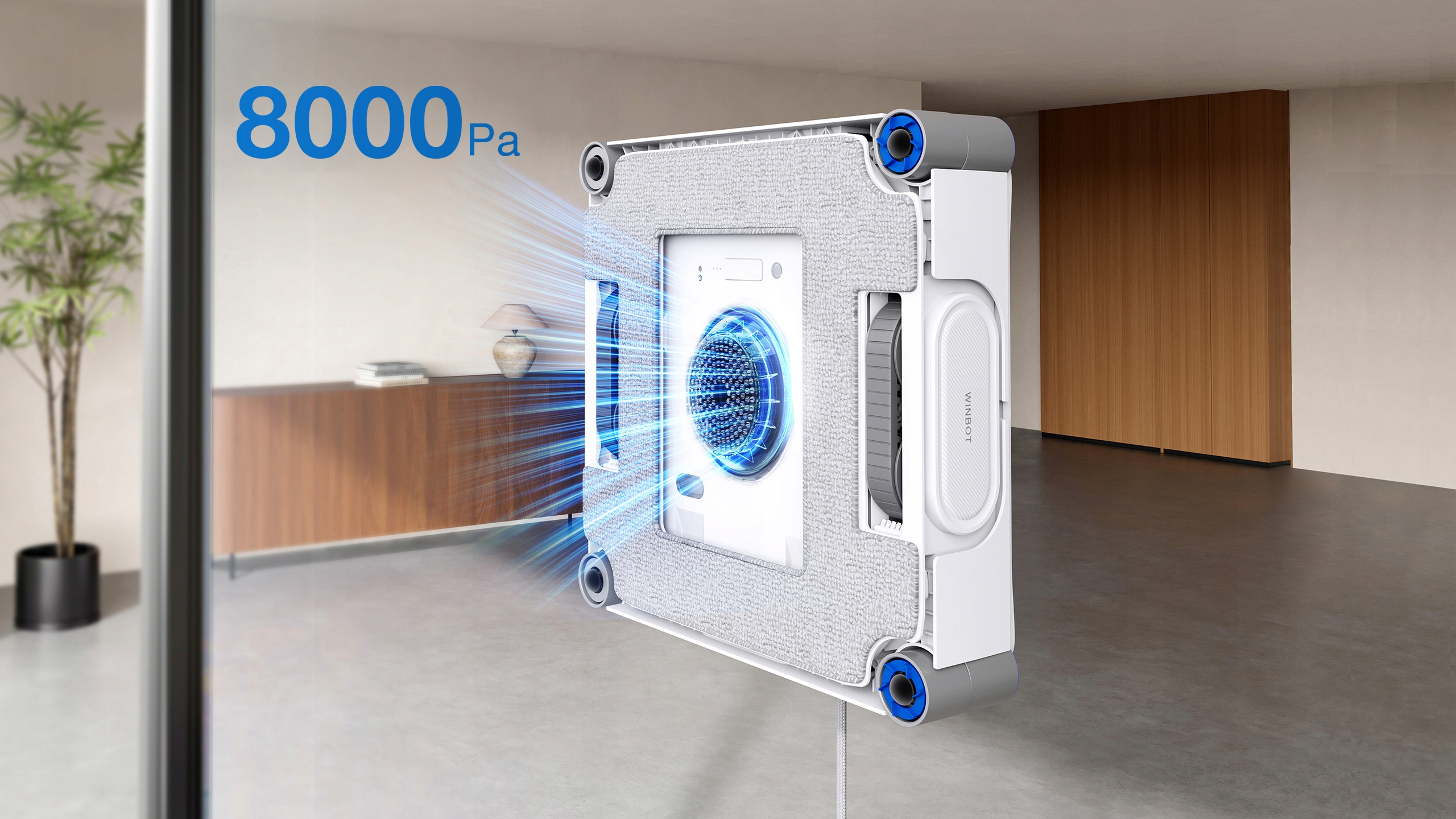 Biały czyścik do okien z niebieskimi akcentami czyści okno. Widoczny jest tekst "8000Pa", a także roślina i drewniane meble.