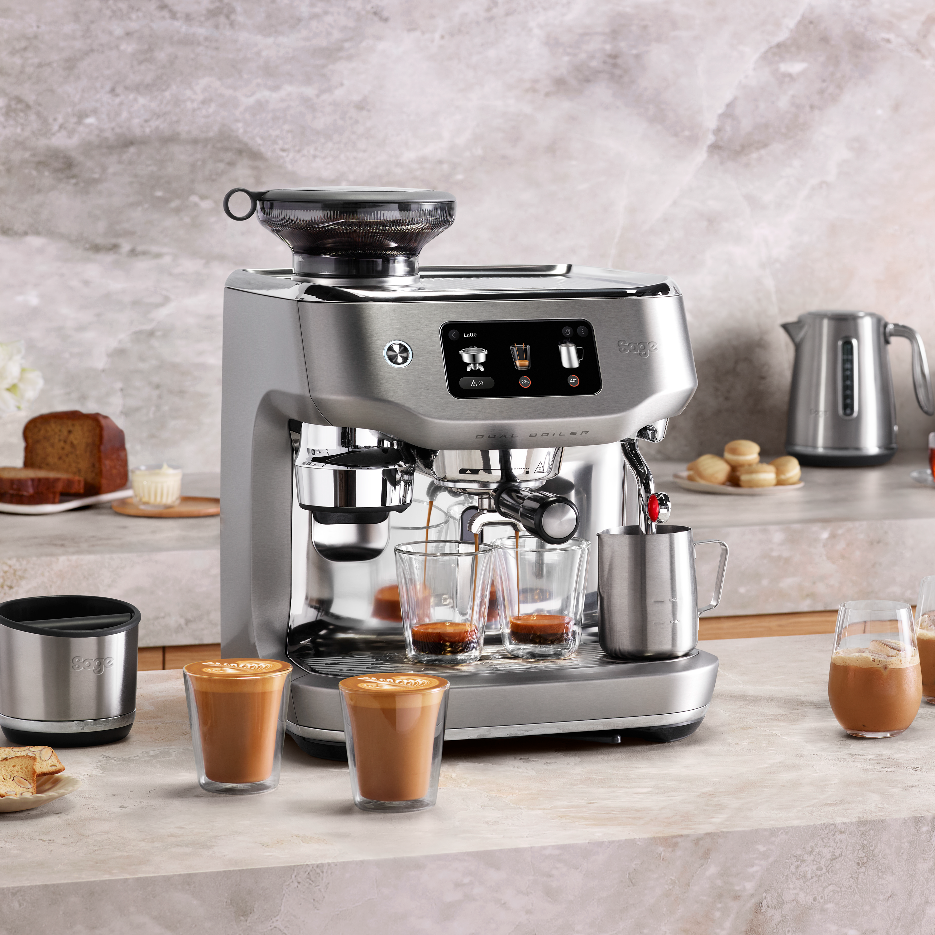 Eine Espressomaschine steht auf einer Theke mit Kaffeegetränken und Gebäck.