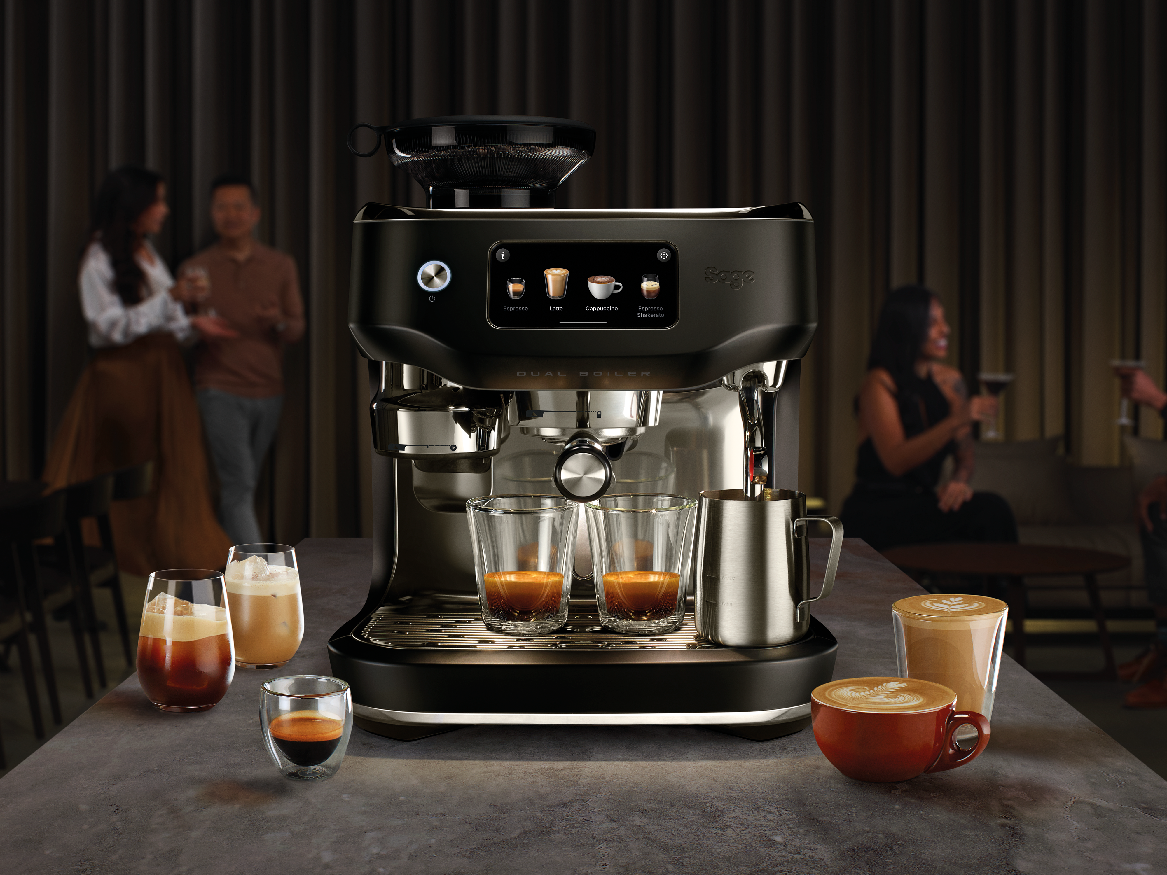 Eine Kaffeemaschine mit Espresso-, Latte- und Cappuccino-Optionen. Auf dem Tisch stehen mehrere Kaffeegetränke, im Hintergrund Personen.