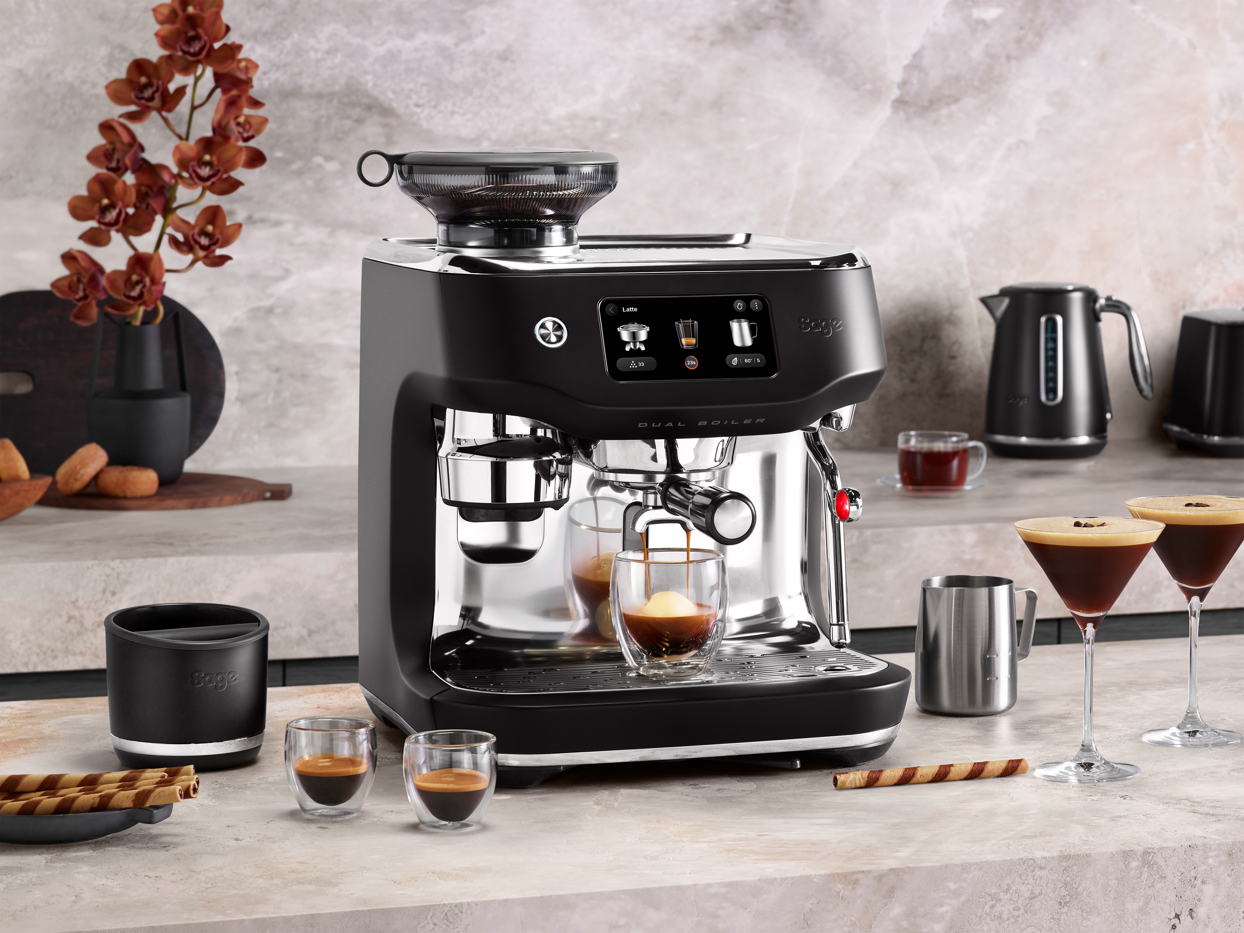 Eine schwarze Espressomaschine, aus der Kaffee gegossen wird. Espressotassen, Kaffee und Snacks auf der Theke.