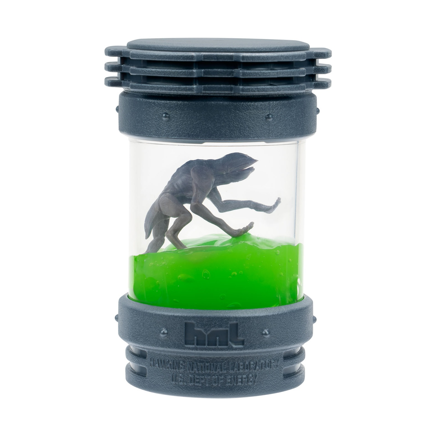 Una figura scura in un contenitore trasparente con liquido verde. Il contenitore ha un coperchio e una base blu scuro con il testo: 'Hawkins National Laboratory'.