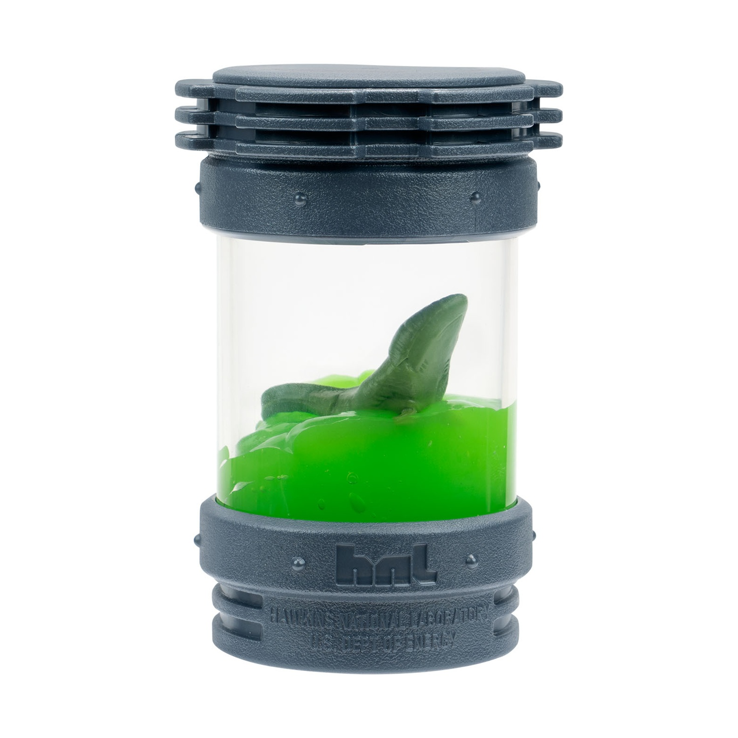 Un contenitore cilindrico contiene una sostanza verde a forma di blob con un oggetto verde all'interno. Il contenitore è grigio scuro con un centro trasparente in plastica.