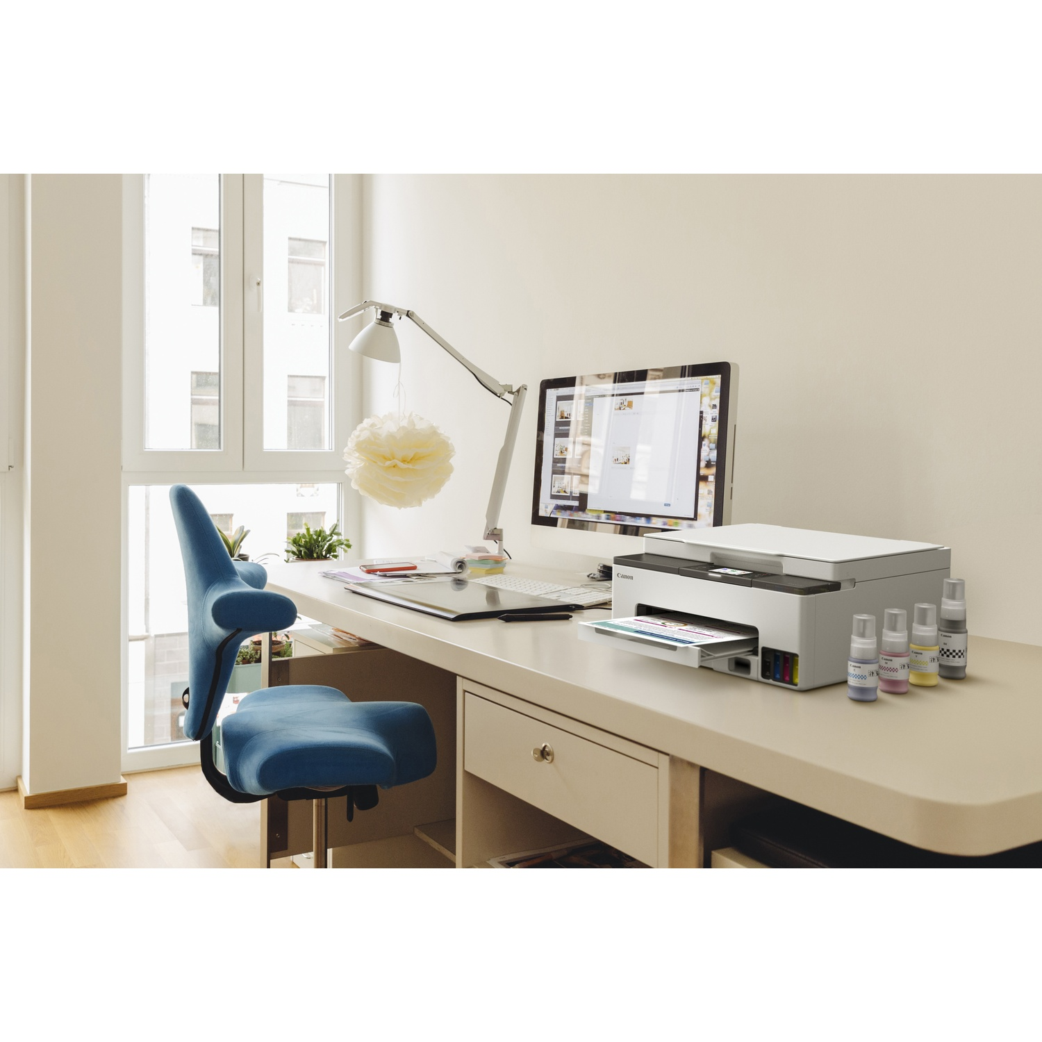 Un bureau avec une imprimante, un ordinateur et des bouteilles d'encre. Une chaise bleue est à proximité. Une fenêtre est en arrière-plan.