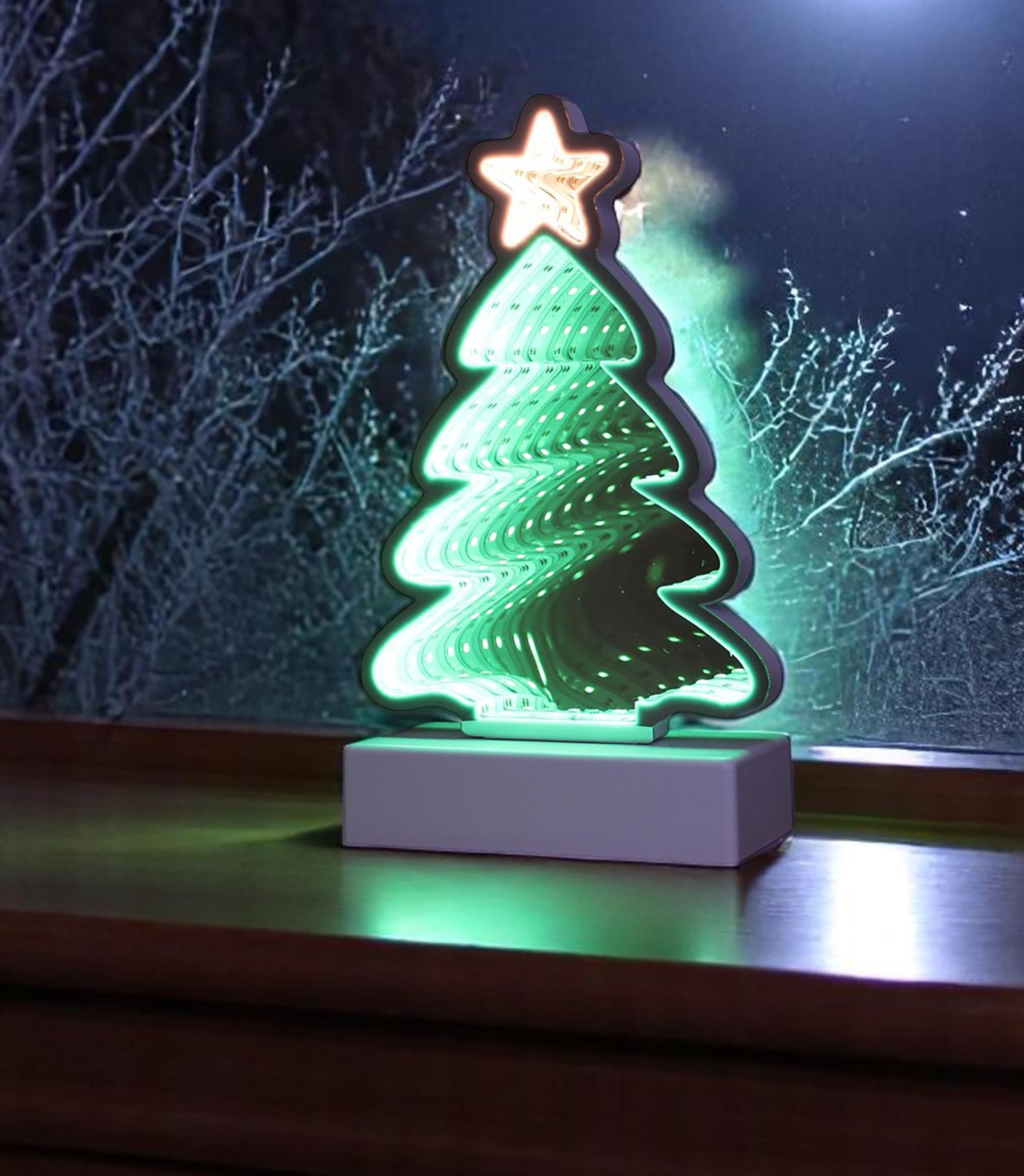 Ein grünes Weihnachtsbaumlicht mit einem Stern oben steht auf einer Holzoberfläche. Im Hintergrund sind kahle Äste zu sehen.