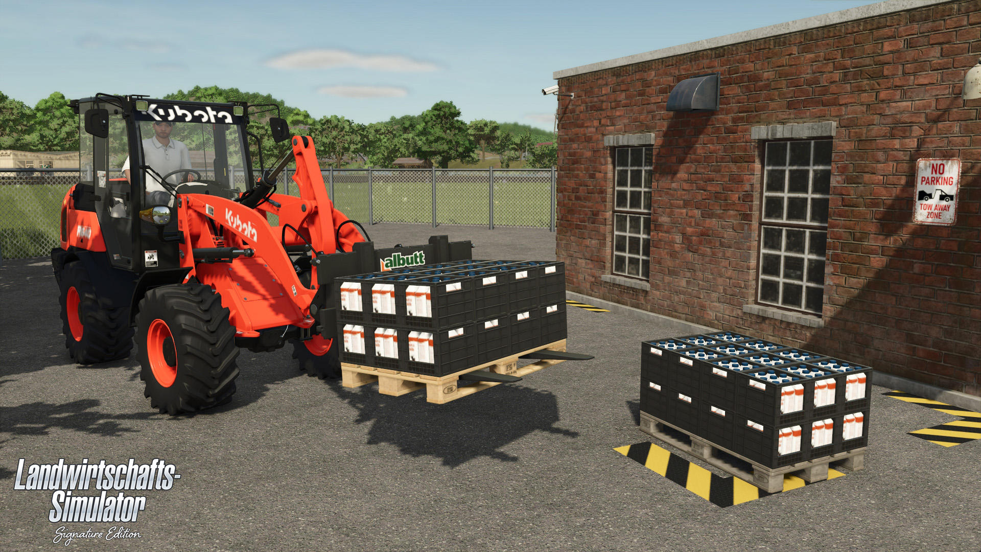 Ein orangefarbener Kubota-Traktor belädt Milchbehälter. Rechts ein Backsteingebäude, im Hintergrund ein Zaun und Bäume.