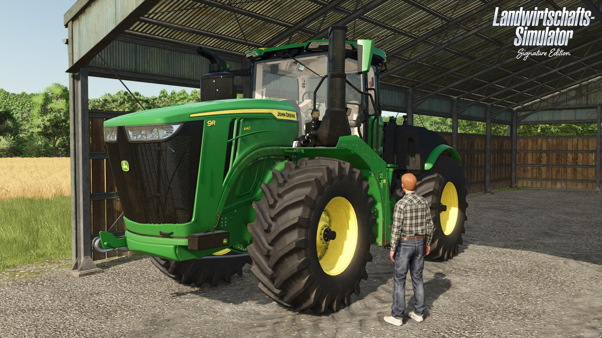 Ein grüner John Deere Traktor steht in einem Schuppen neben einem Mann. Der Traktor hat große Reifen, und der Schuppen besteht aus Metall.