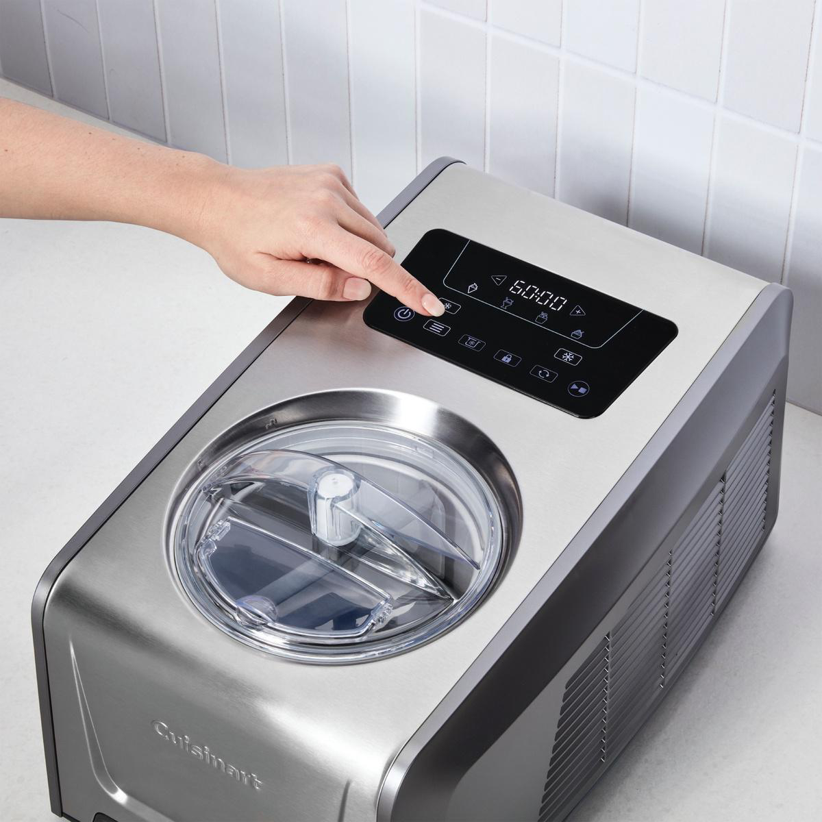 Eine Hand drückt einen Knopf auf einer silbernen Eismaschine. Ein digitales Display und ein klarer Deckel sind sichtbar.