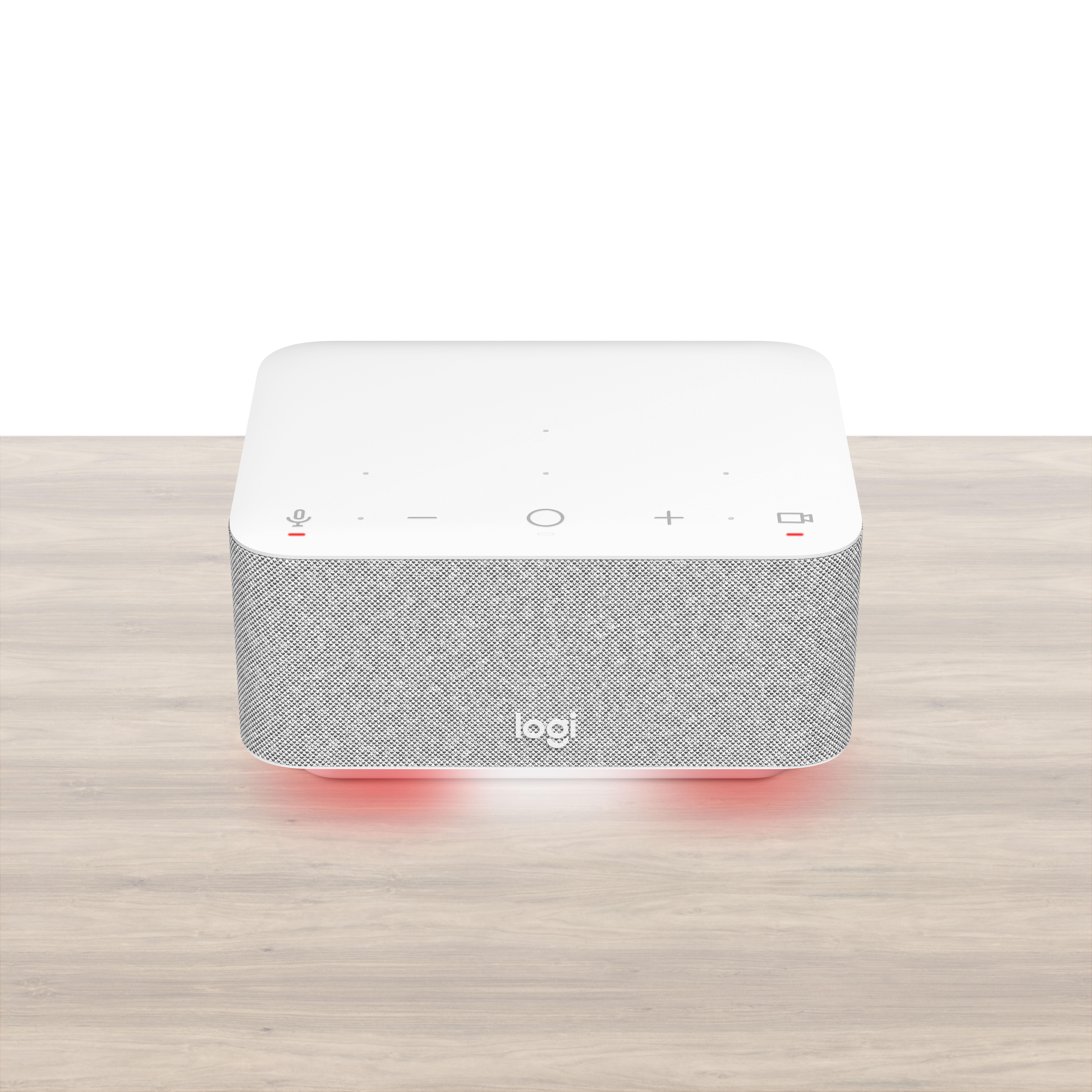 Ein weißer Smart-Lautsprecher mit grauem Lautsprechergrill auf einem Holztisch mit roten Lichtern. Das Logitech-Logo ist sichtbar.