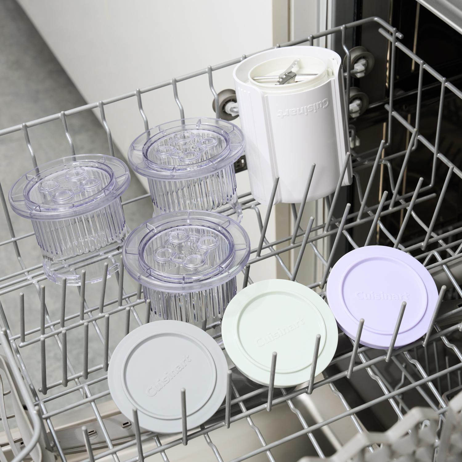 Cuisinart-Küchenmaschinenteile in einem Geschirrkorb. Klare Behälter, Deckel in Grau, Grün und Lila sowie ein weißes Maschinenteil.