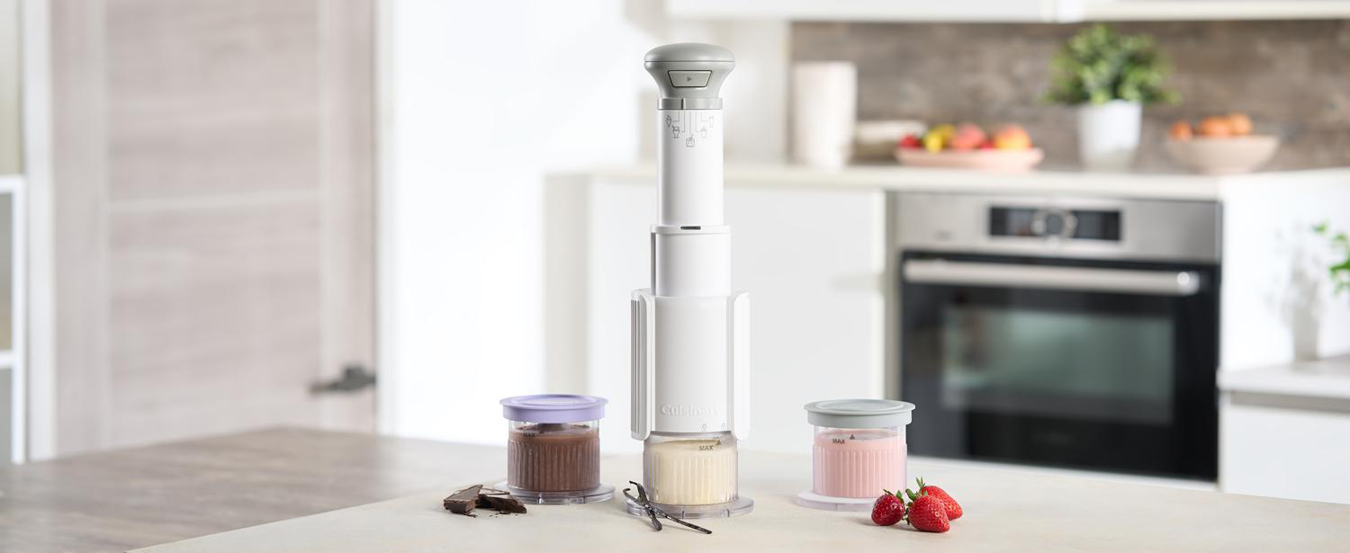Ein weißes Küchengerät mit drei Gläsern mit Inhalt, Schokolade, Vanille und Erdbeere. Erdbeeren und Vanilleschoten liegen neben Gläsern.