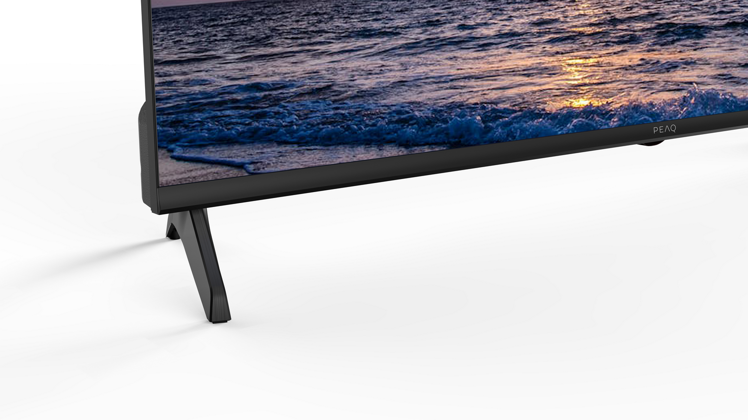 Un televisor negro con patas. La pantalla muestra un paisaje marino. El televisor está sobre una superficie blanca.