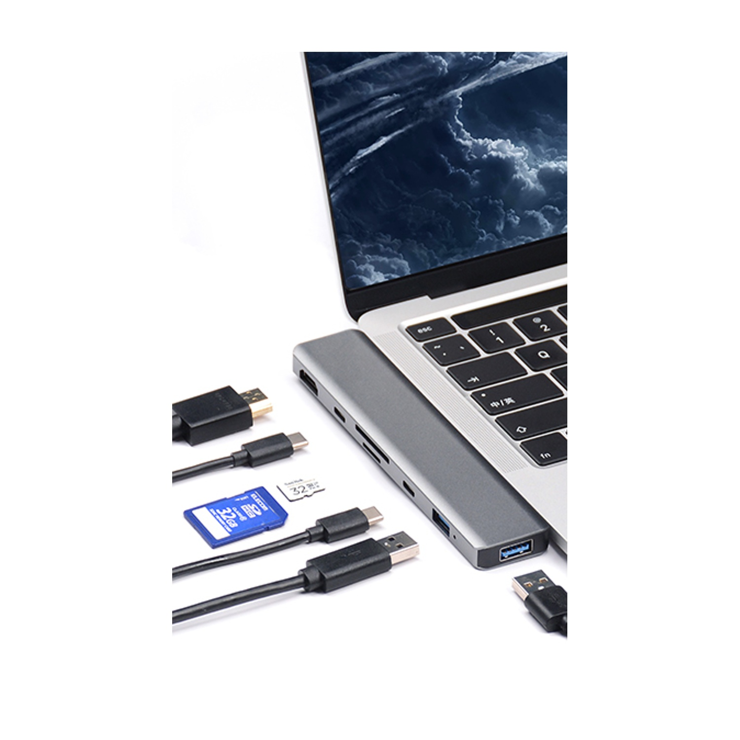 Laptop con hub collegato, cavi e scheda SD. Lo schermo del laptop mostra un cielo nuvoloso. Sono visibili vari connettori.