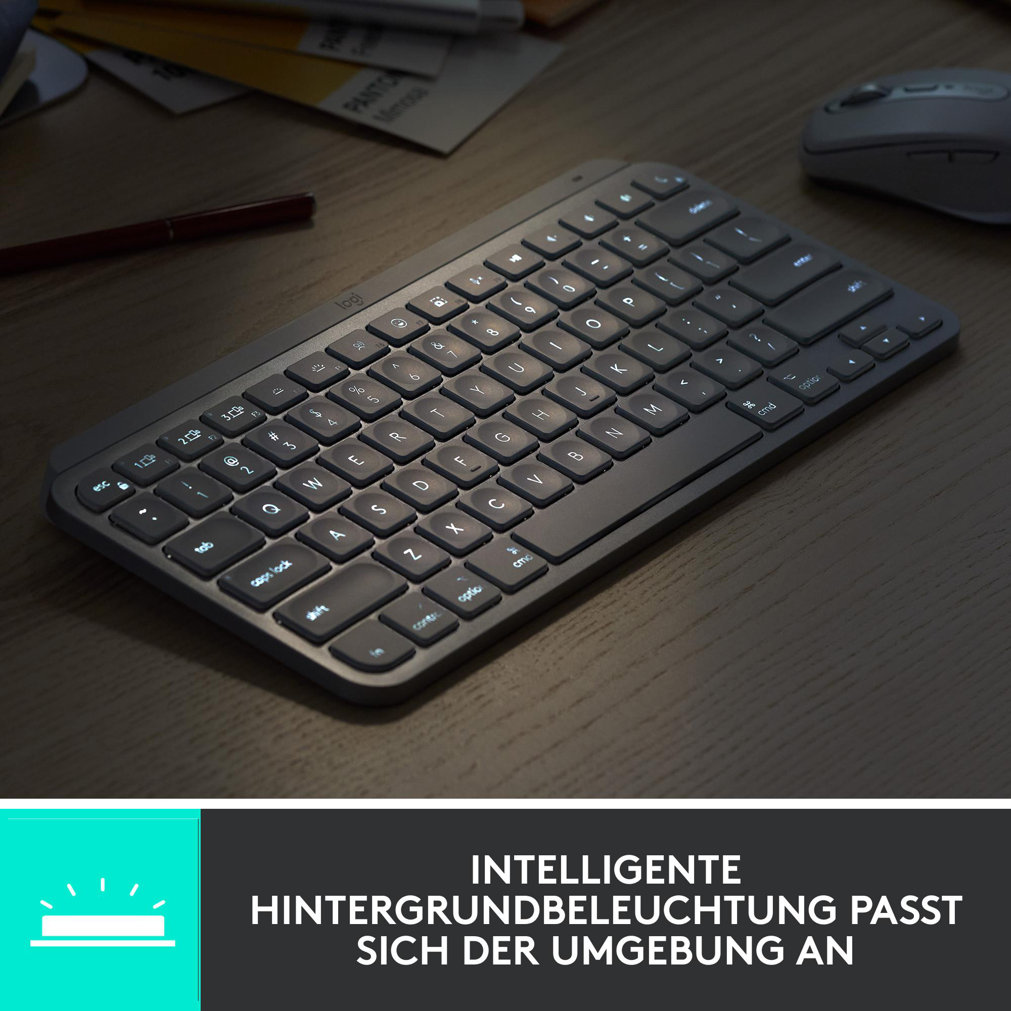 Dunkelgraue Tastatur mit beleuchteten Tasten auf Holzschreibtisch. Maus und Stift sind ebenfalls sichtbar.
