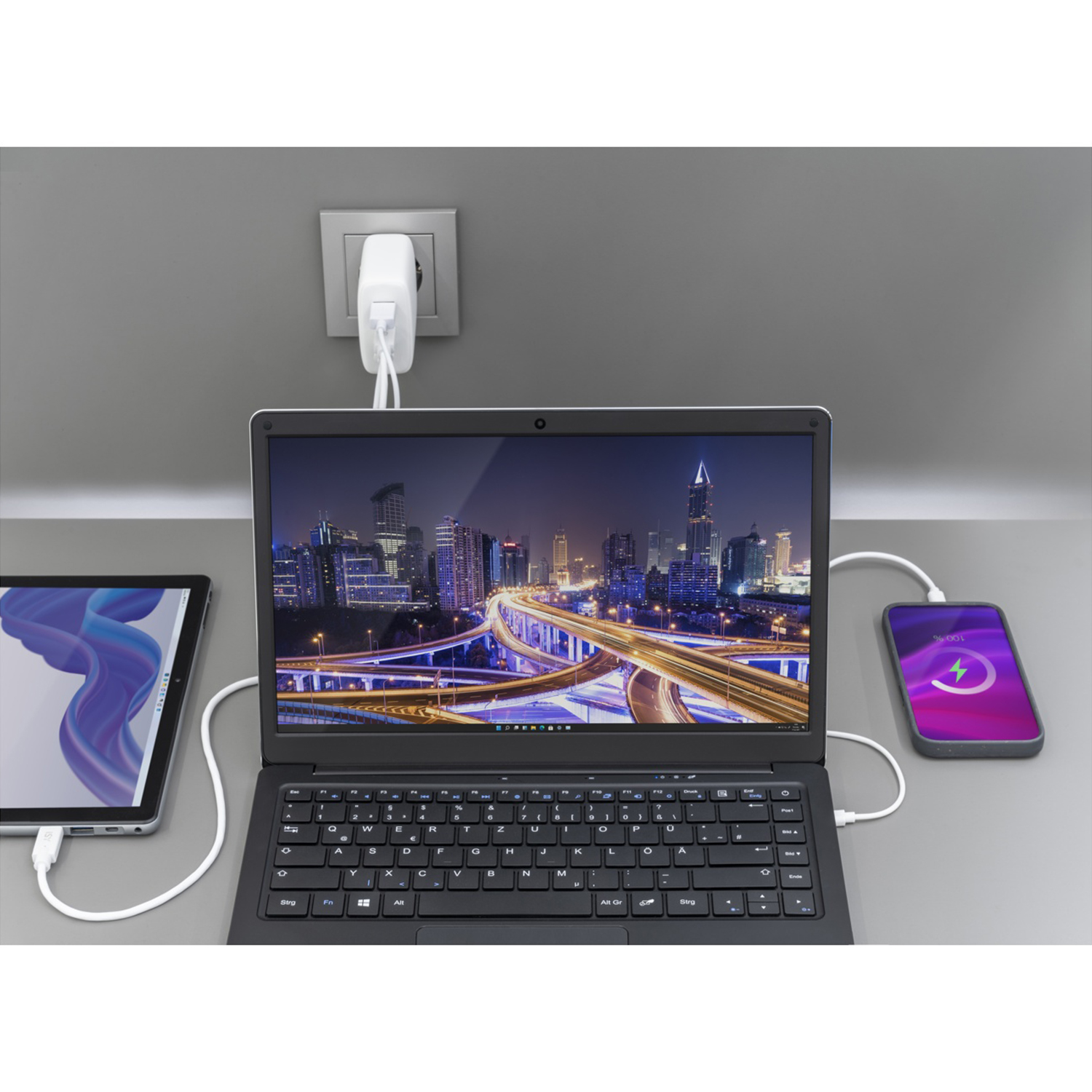 Laptop, tablet e telefono in carica. Sfondo del paesaggio urbano sullo schermo del laptop. Presa di corrente sullo sfondo.