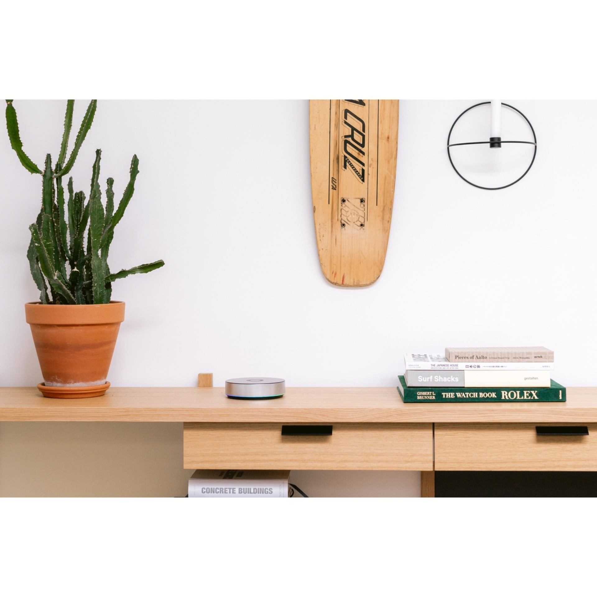 Un escritorio de madera con un cactus, libros, una patineta y un altavoz inteligente.