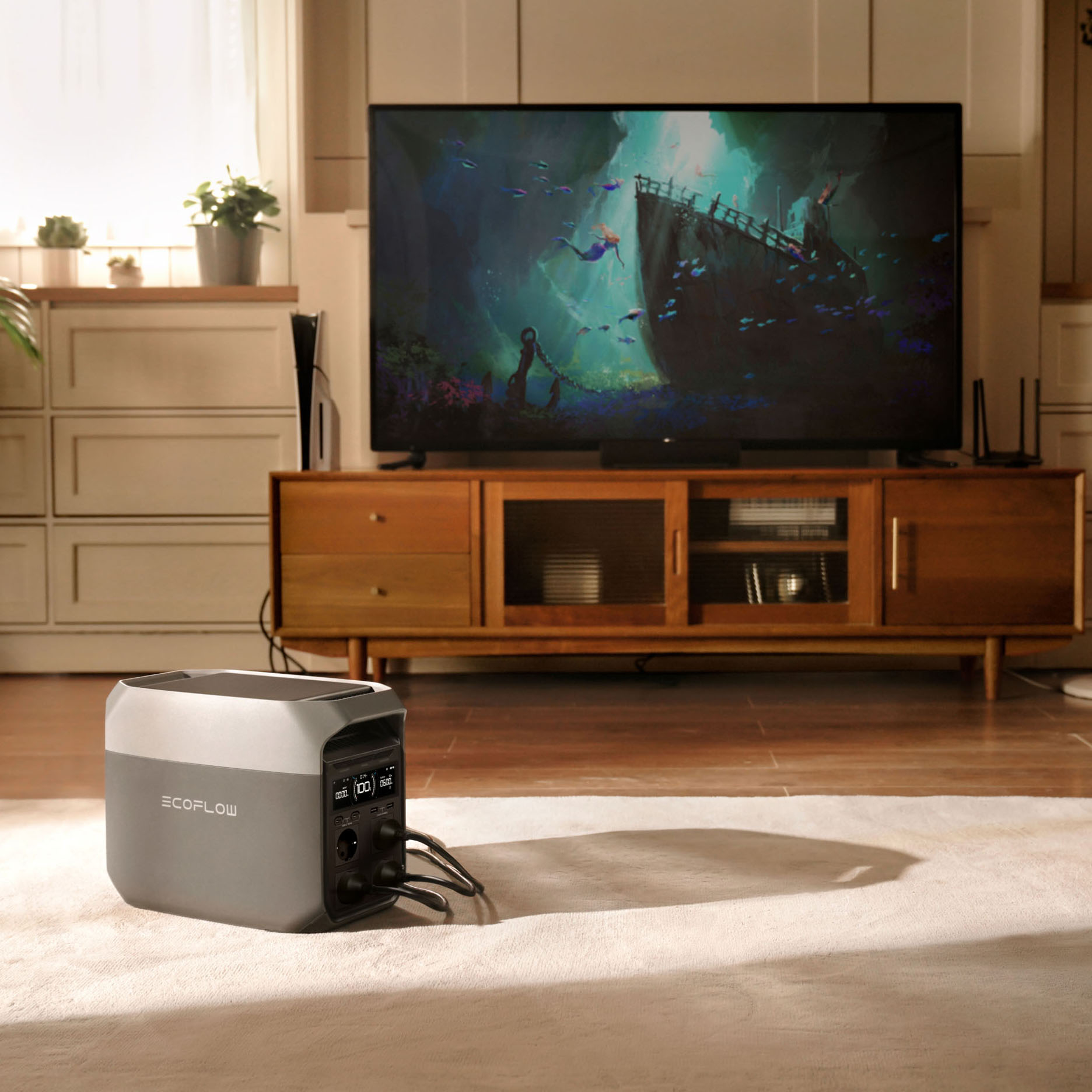 Una estación de energía EcoFlow gris sobre una alfombra. Un televisor muestra una escena submarina. Se ven un mueble y plantas.