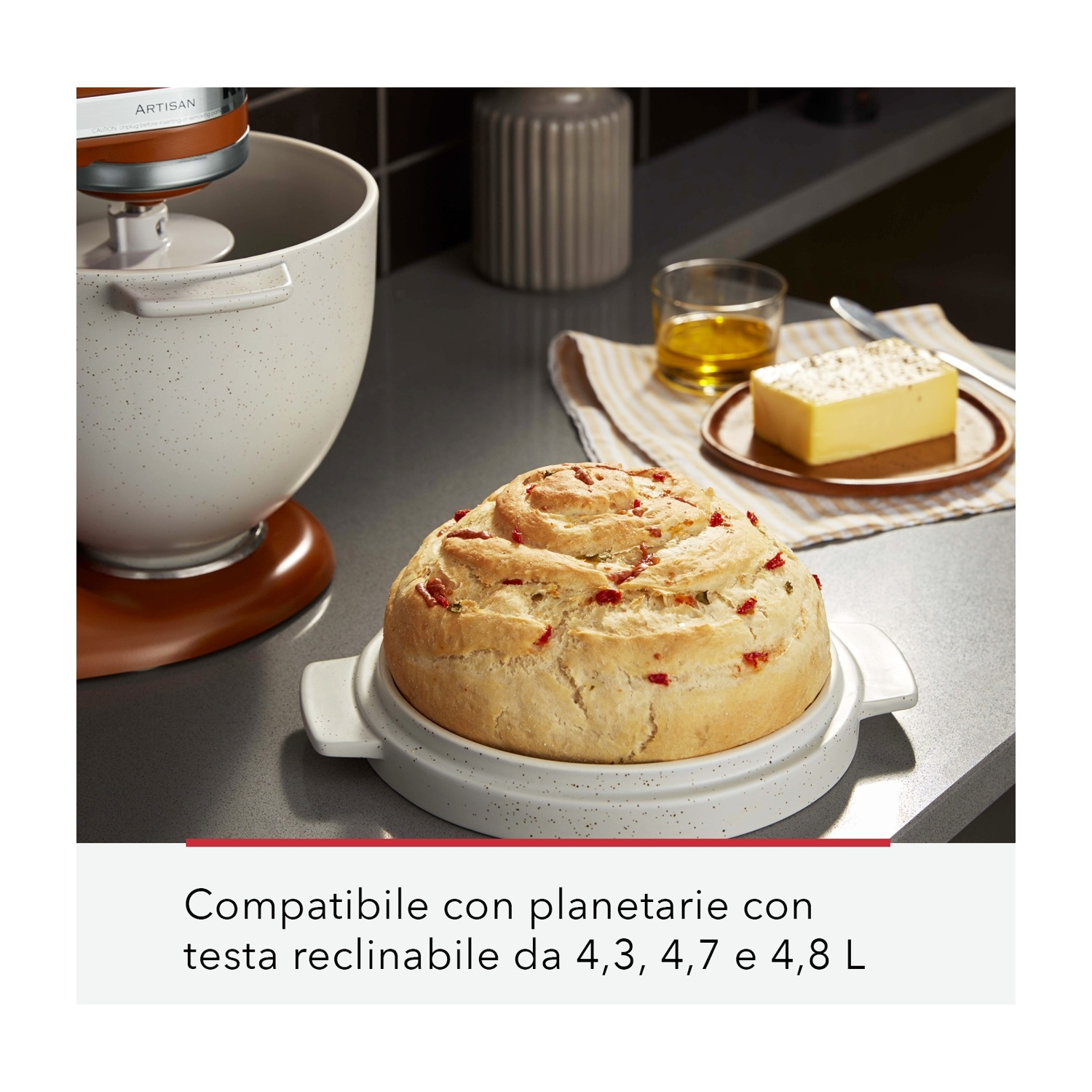Pane su piatto bianco, mixer KitchenAid, burro e olio su un bancone.