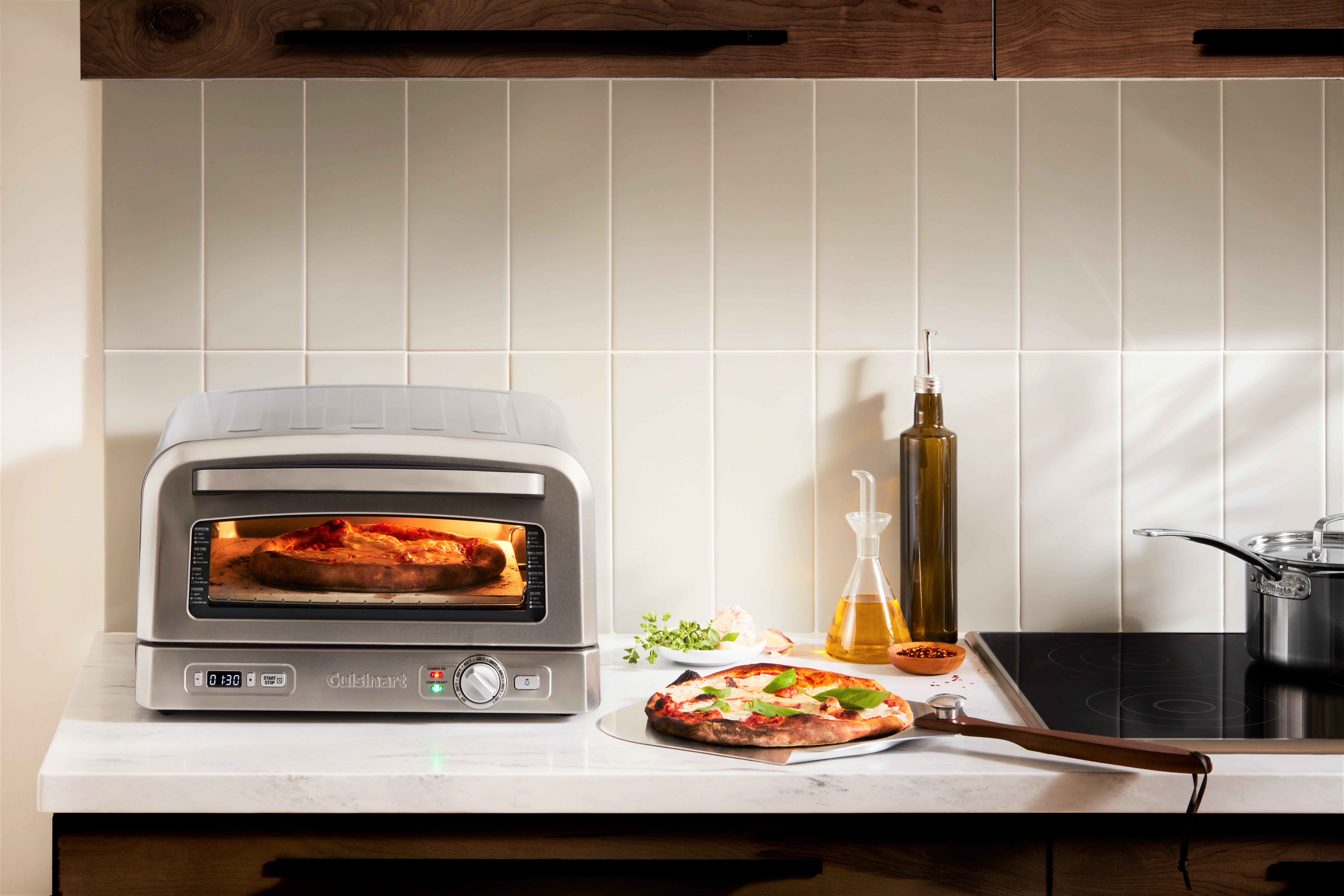 Ein Pizzaofen mit Pizza. Eine fertige Pizza liegt auf einer Theke neben einer Pfanne und Olivenöl.