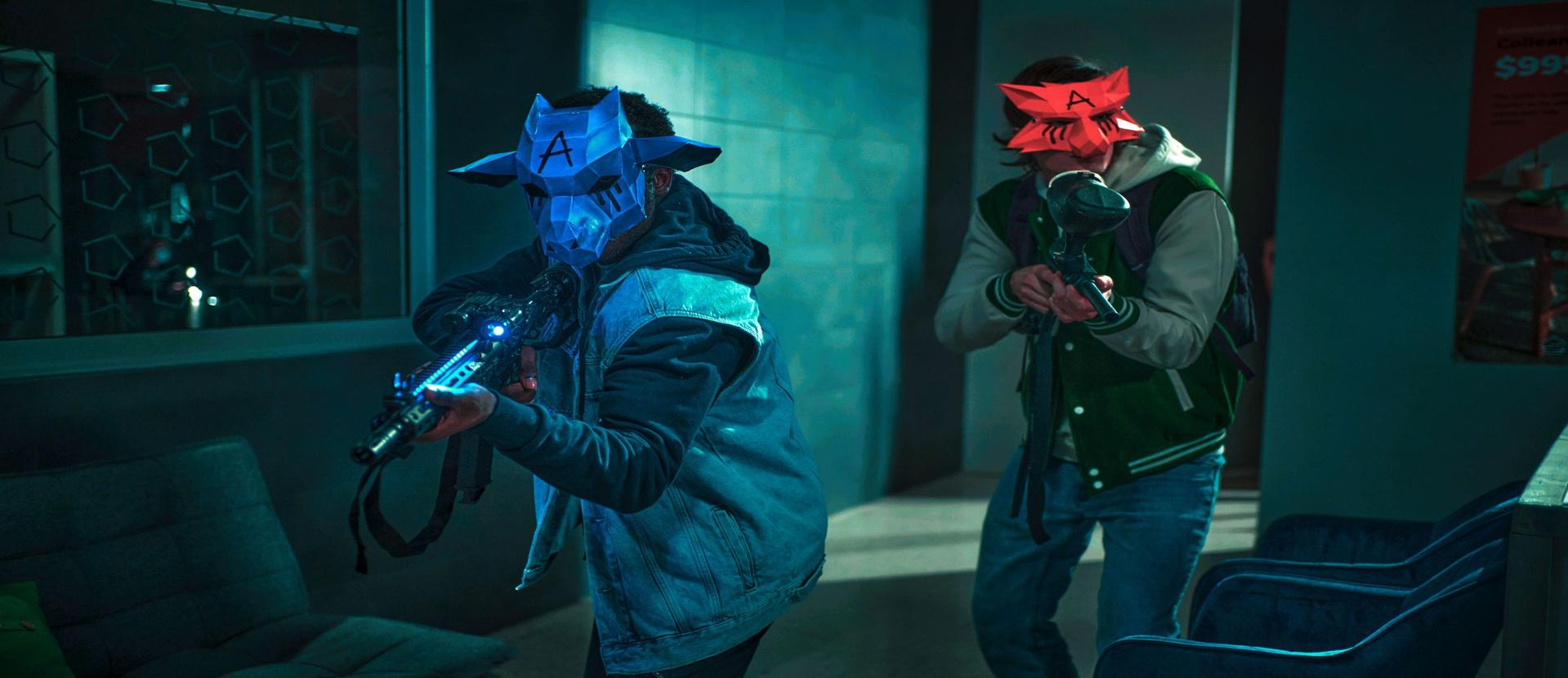 Zwei maskierte Personen mit Waffen. Einer trägt eine blaue Maske mit einem A, der andere eine rote Maske. Beide in einem dunklen Raum.