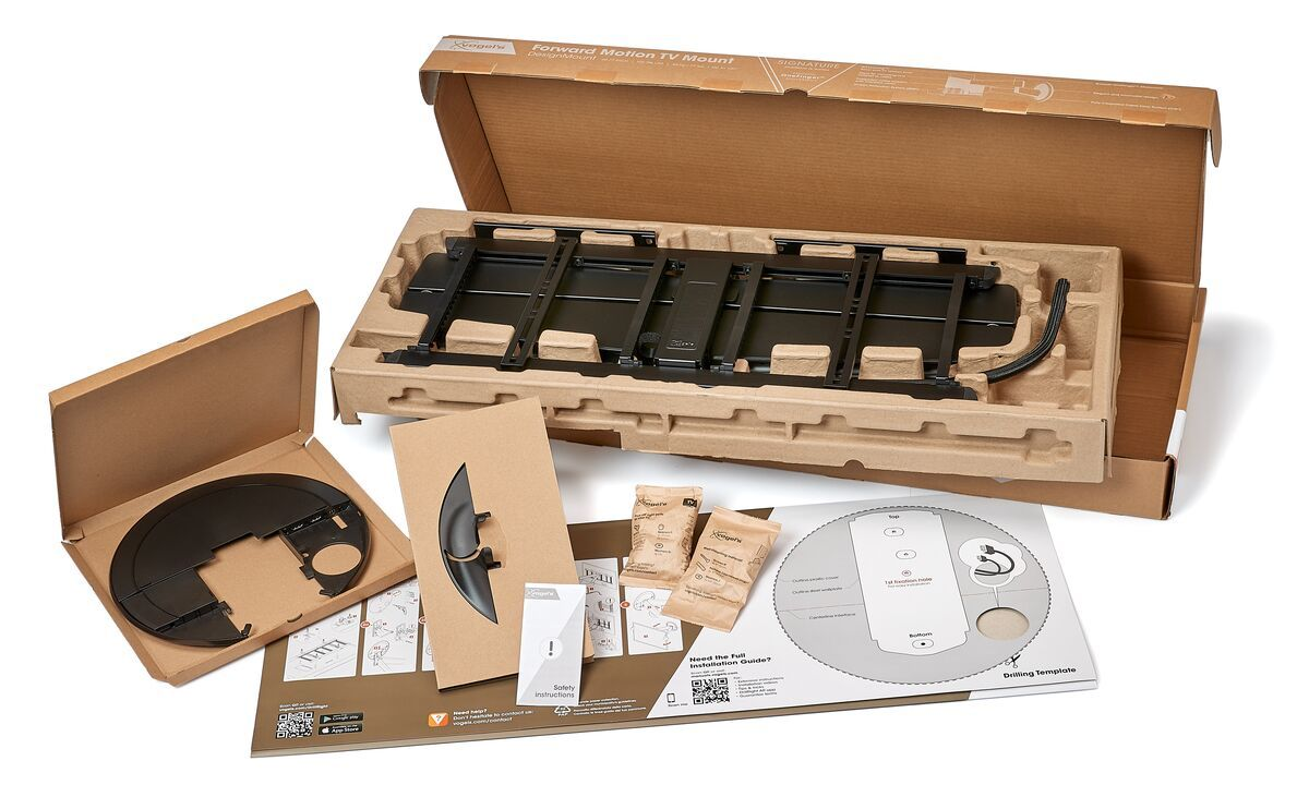 Otwarta skrzynia do montażu telewizora z czarnym uchwytem, papierami i sprzętem. Widoczne brązowe kartony i opakowania.