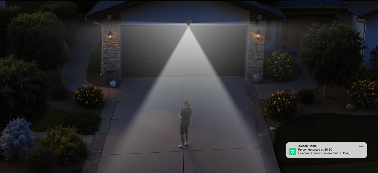 Osoba stoi na oświetlonym podjeździe w nocy. Kamera bezpieczeństwa nad garażem wykrywa osobę.