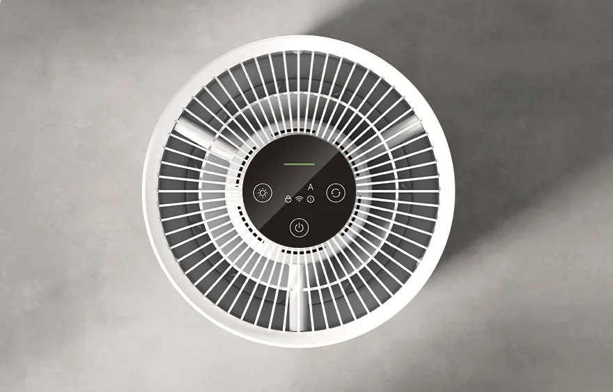 Widok z góry na biały oczyszczacz powietrza na szarej powierzchni. Ma okrągłą konstrukcję z panelem sterowania i łopatkami wentylatora.