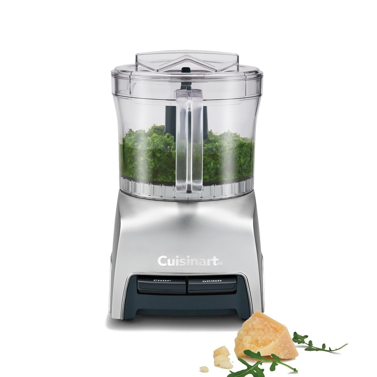 Ein Cuisinart-Foodprozessor mit grün gehacktem Essen. Parmesan und Rucola liegen im Vordergrund.