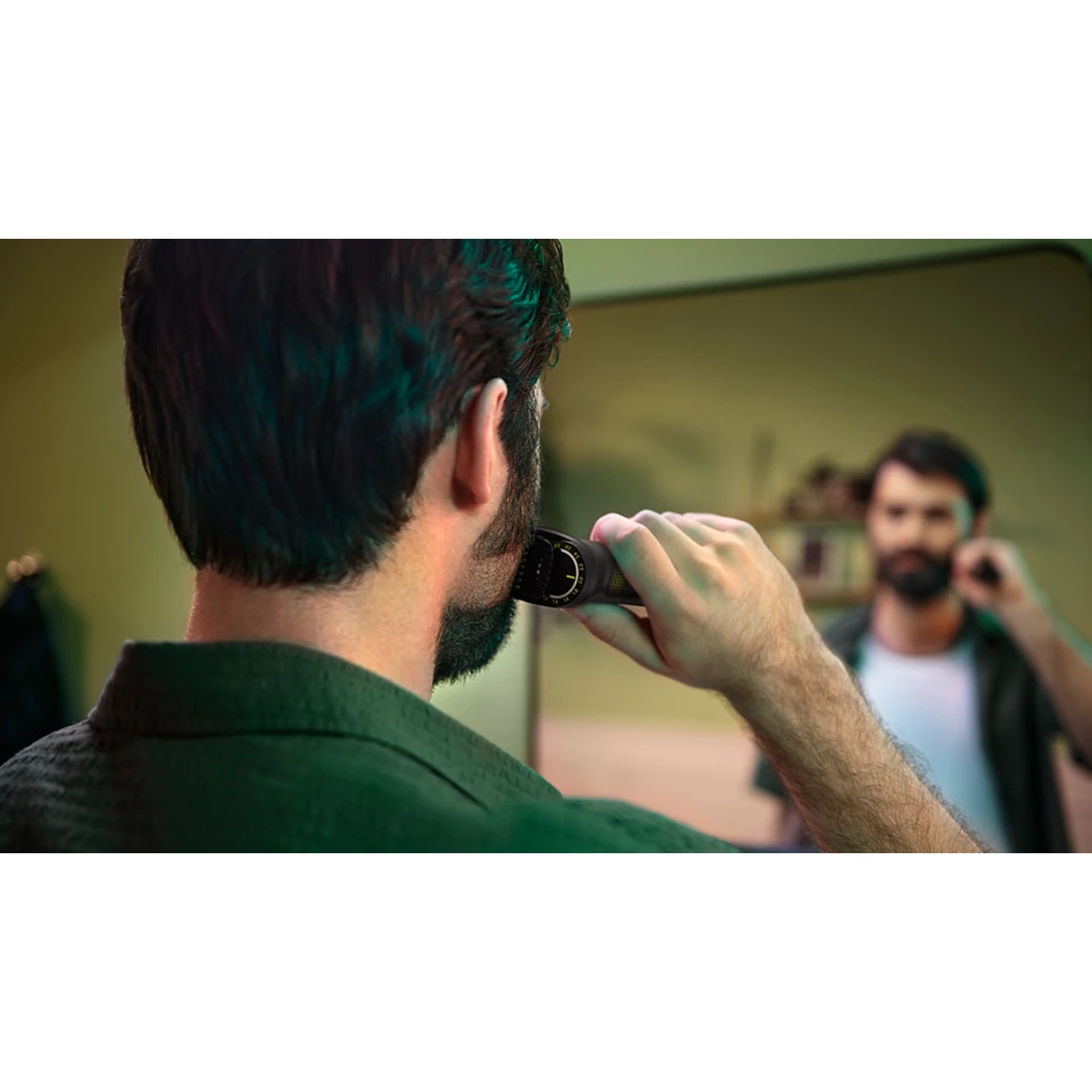 Un uomo si rade la barba con un rasoio elettrico davanti a uno specchio. Lo specchio riflette l'uomo e l'interno della stanza.