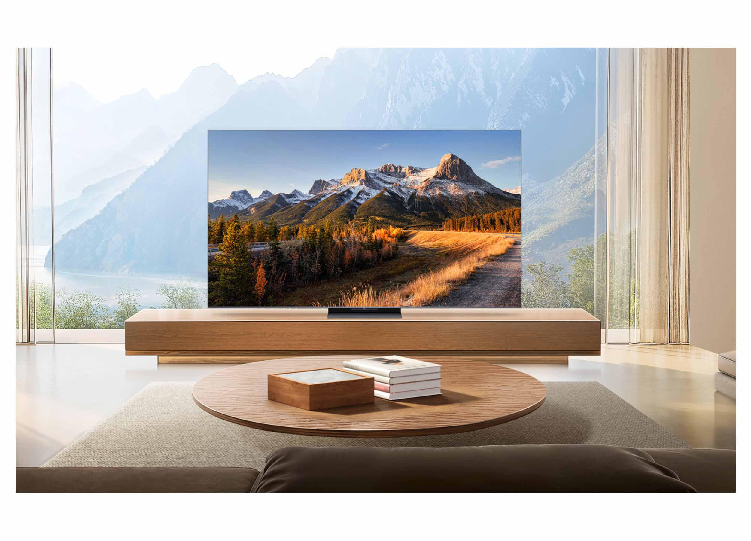 Ein Fernseher zeigt eine Berglandschaft. Ein Holztisch hat Bücher und eine Box. Ein Fenster zeigt Berge.