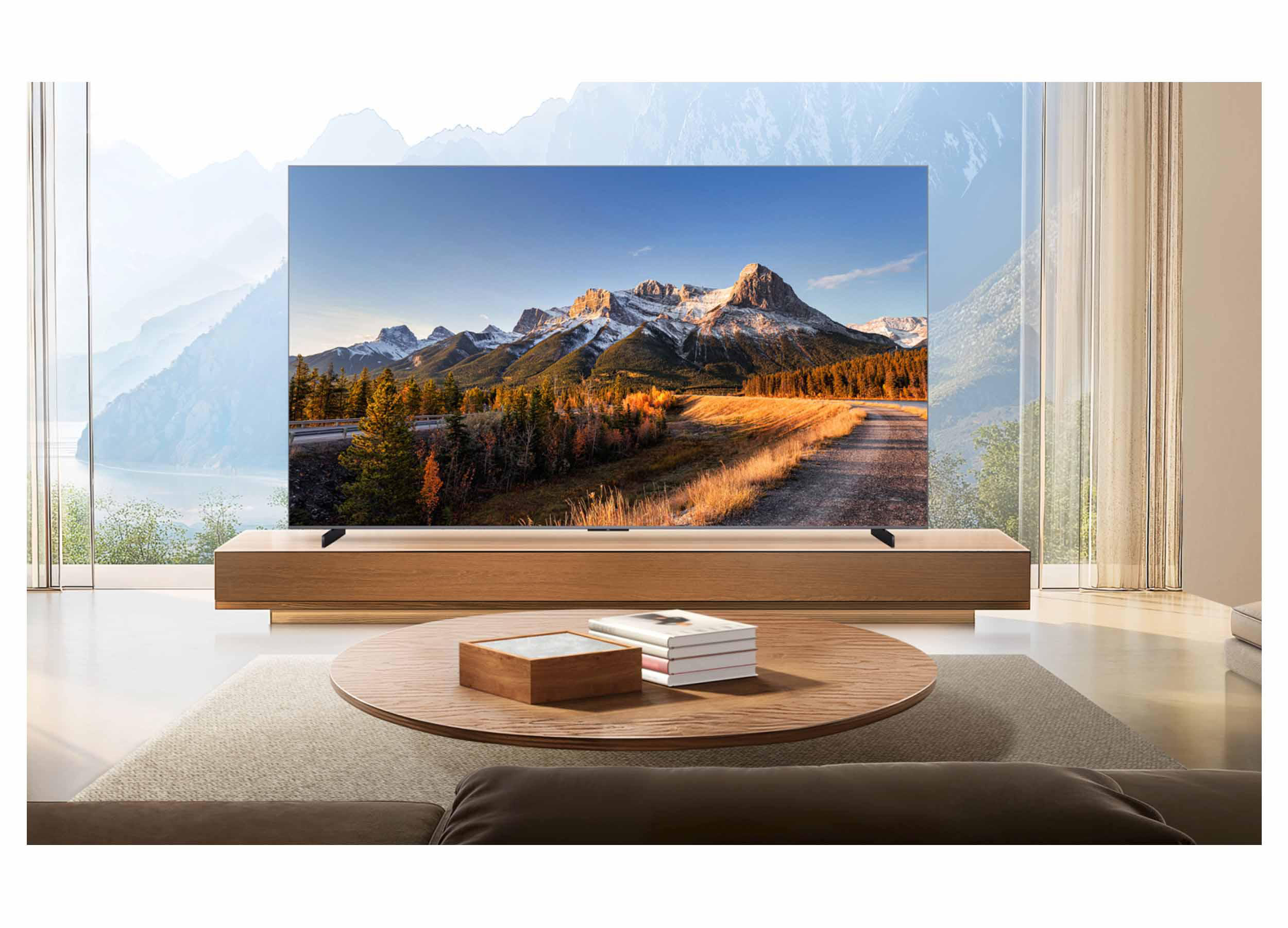 Wohnzimmer mit Fernseher, der eine Berglandschaft zeigt. Ein Couchtisch, Bücher und ein Sofa sind im Vordergrund.