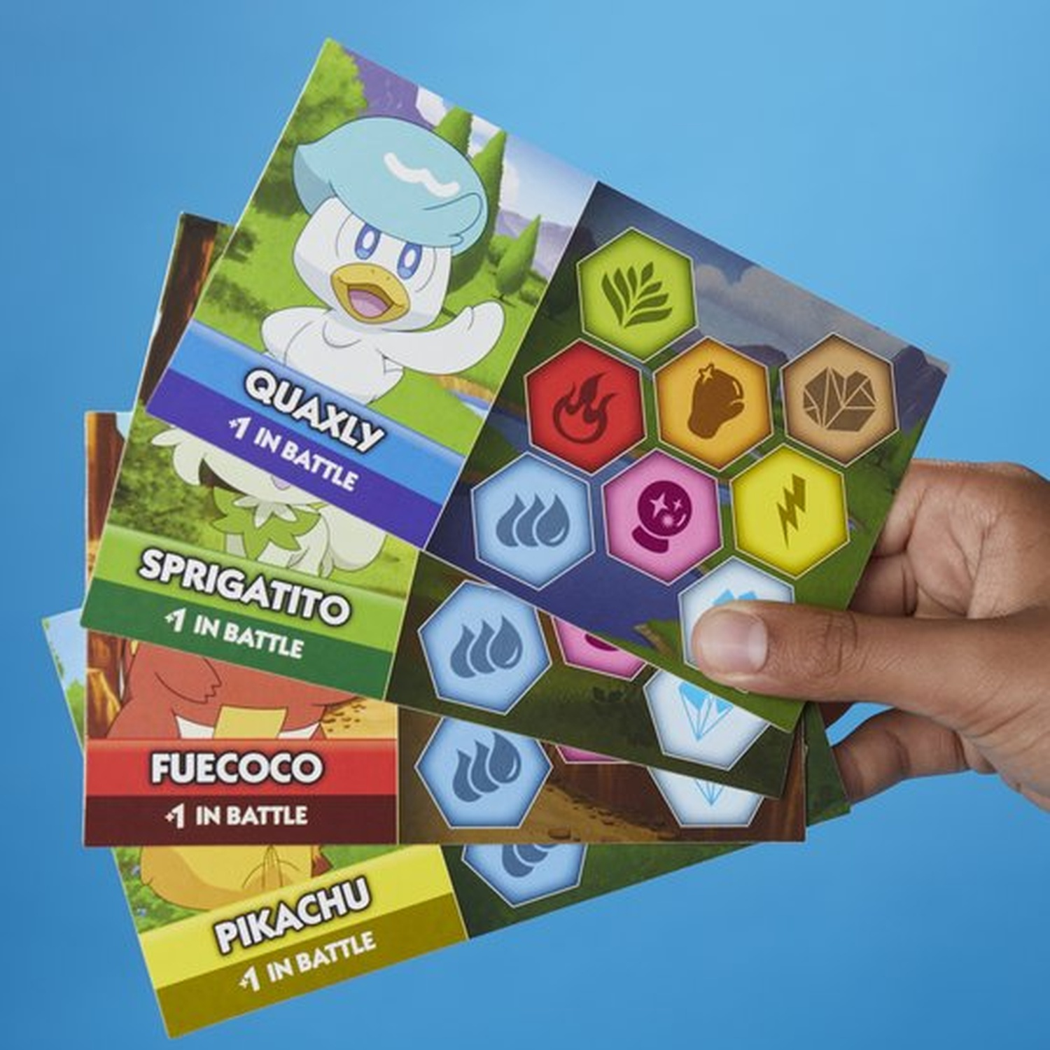 Hand die Pokémon-kaarten vasthoudt met Quaxly, Sprigatito, Fuecoco en Pikachu. Diverse gekleurde zeshoekige symbolen aan de rechterkant.