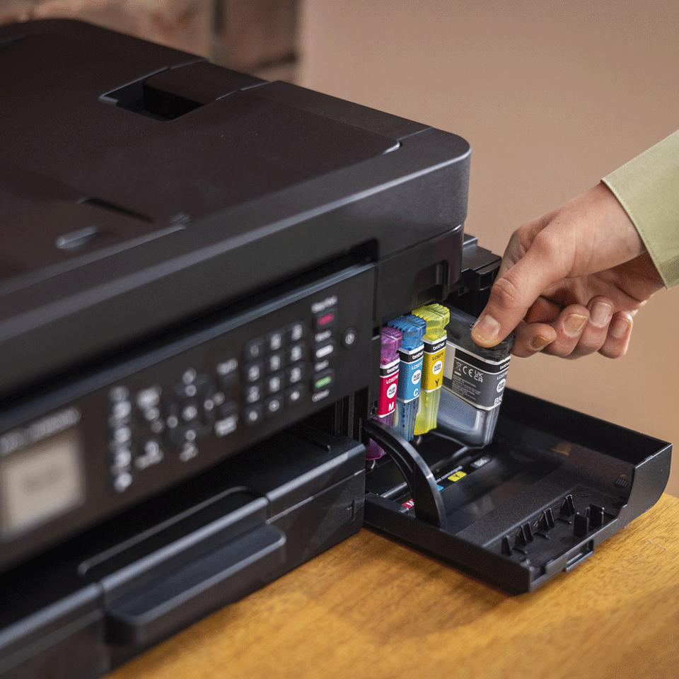 Eine Hand setzt eine schwarze Tintenpatrone in einen schwarzen Drucker ein. Andere farbige Patronen sind bereits eingesetzt.