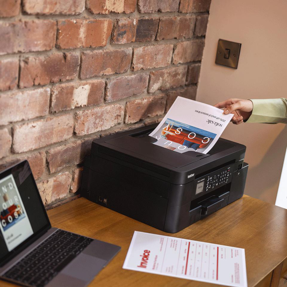 Ein Drucker druckt ein Papier mit 'Sofa-Verkauf'. Ein Laptop und eine Rechnung liegen auf dem Holztisch. Eine Hand legt das Papier ab.