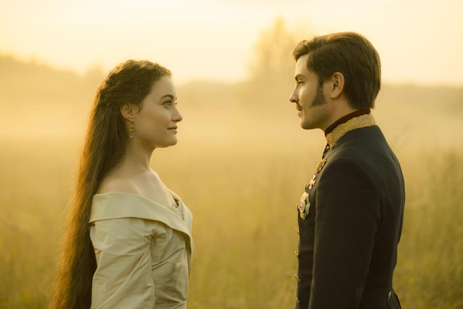 Ein Mann in Uniform und eine Frau in einem cremefarbenen Kleid stehen sich auf einem Feld gegenüber. Der Hintergrund ist ein verschwommenes, goldenes Licht.