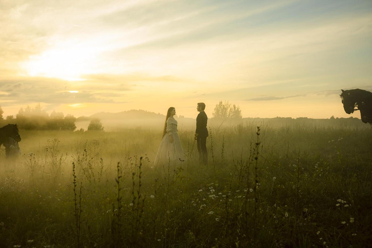 Ein Paar steht bei Sonnenuntergang auf einem Feld. Pferde sind auf beiden Seiten. Der Himmel ist golden mit Nebel.