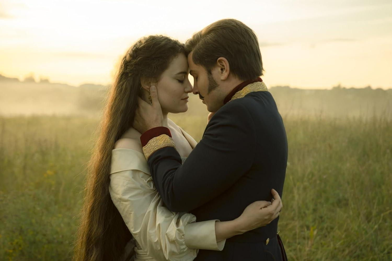 Ein Paar umarmt sich auf einem Feld. Sie sind in historischer Kleidung gekleidet. Der Mann trägt eine dunkle Uniform, die Frau ein cremefarbenes Kleid.