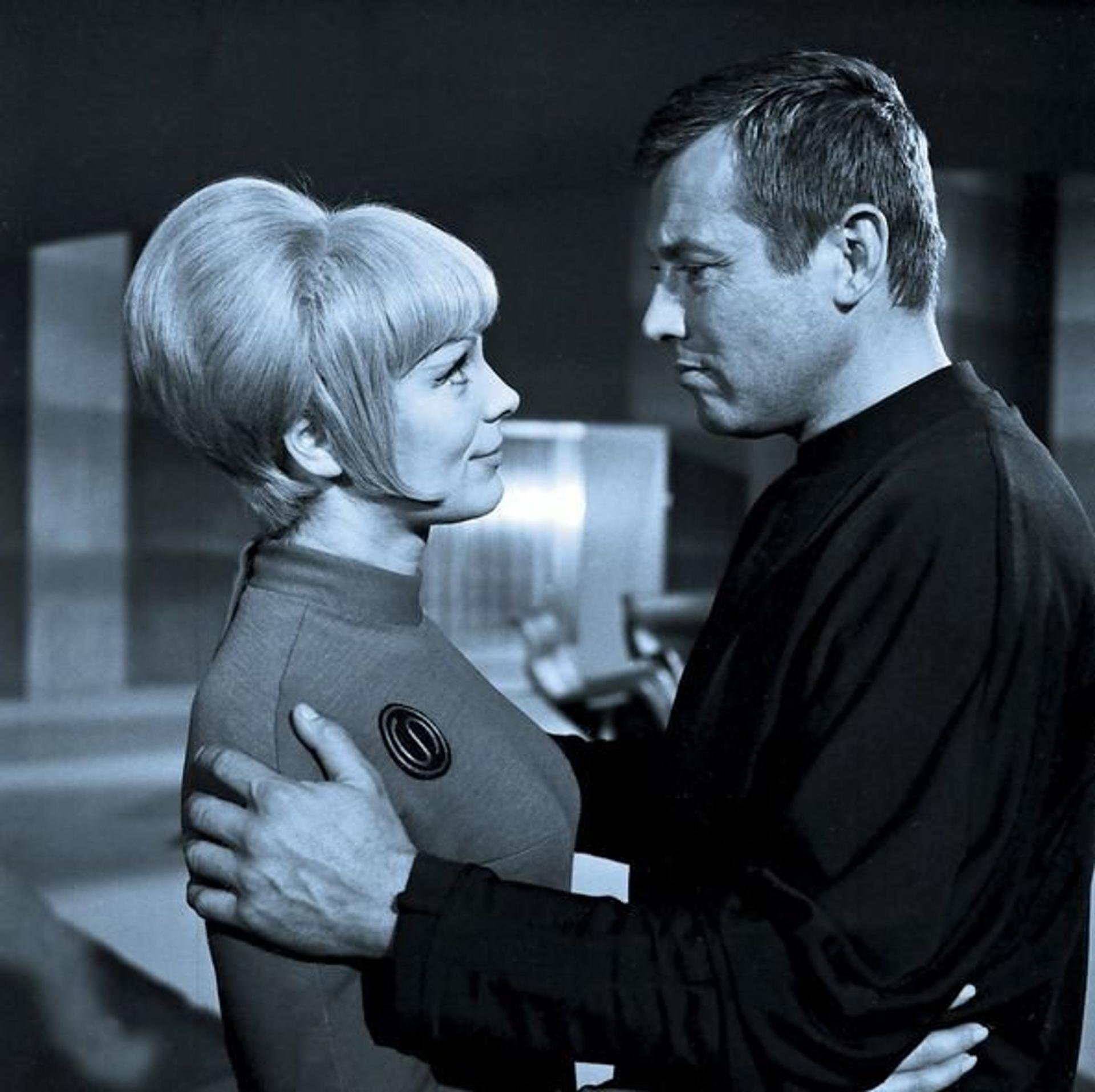 Ein Mann und eine Frau stehen sich gegenüber. Der Mann hat die Arme um die Frau. Beide sehen sich in einer Szene von Star Trek an.