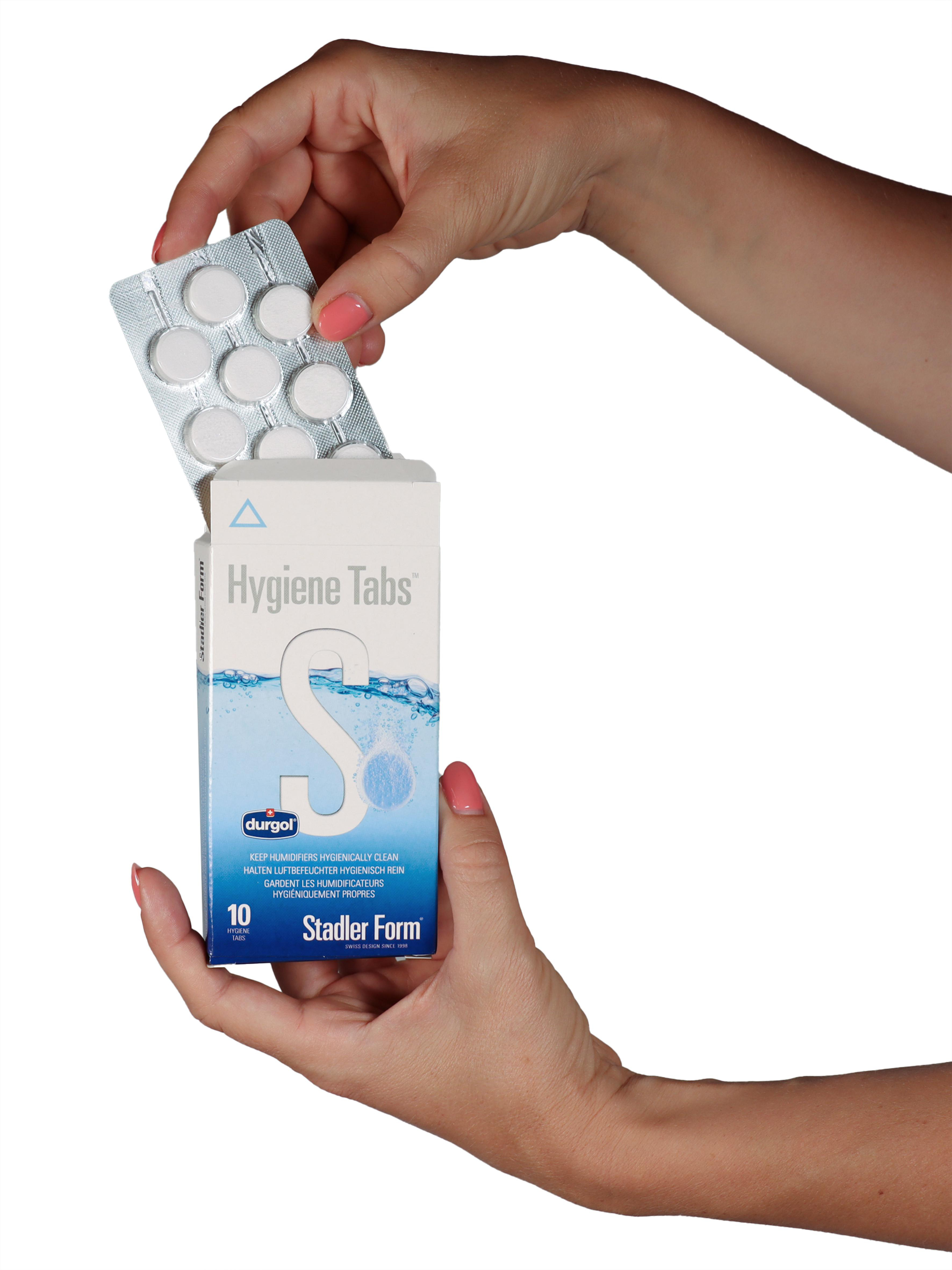 Hände halten eine Schachtel Hygiene Tabs und eine Blisterpackung mit Tabletten. Die Tabletten sind weiß.