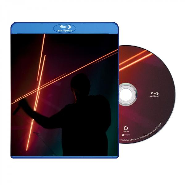 Eine Blu-ray-Hülle mit einer Silhouette einer Person, die ein Mikrofon hält, beleuchtet von orangen Linien. Daneben eine CD.