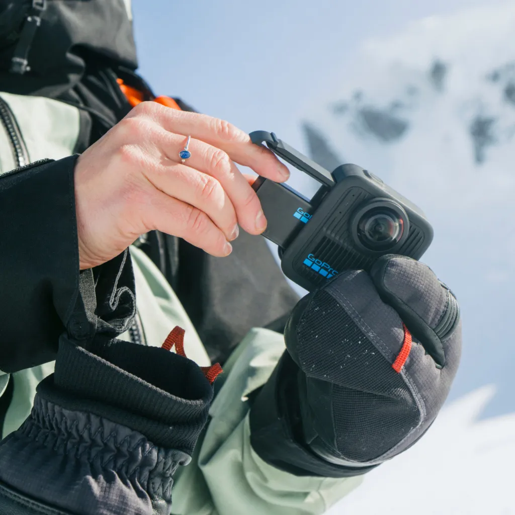 Személy GoPro kamerát tart a havas hegyekben. Kesztyűt és kabátot visel. A gyűrű látható az ujján.