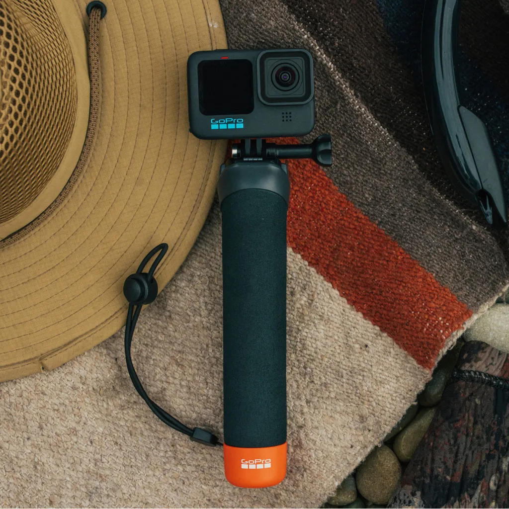 GoPro kamera egy fogantyún. Egy bézs kalap balra. A kamera egy színes takarón van.